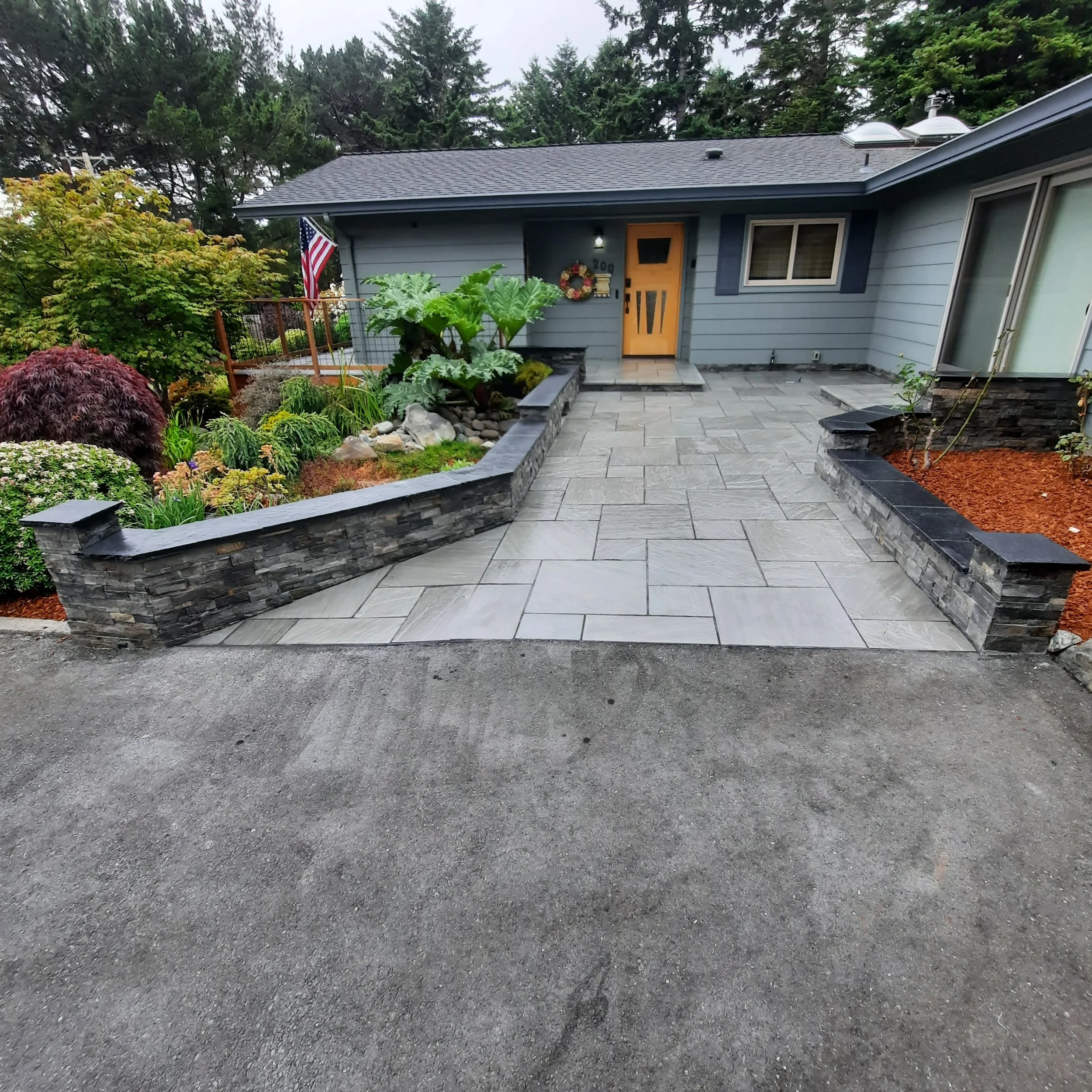 Stone-paved front entry landscape with planting beds and retaining wall.