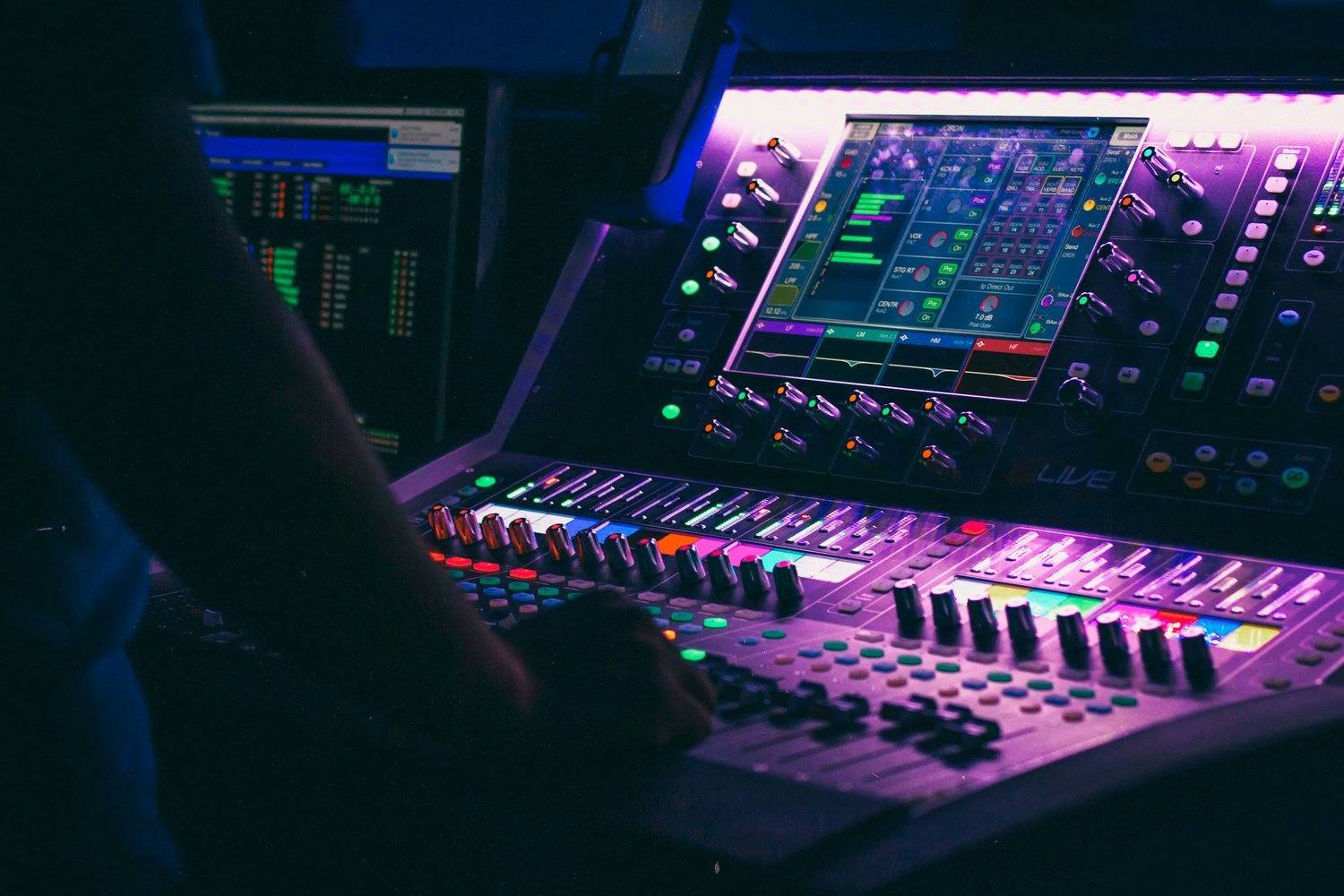 Audio engineer mixing live sound on a lit digital console at an event