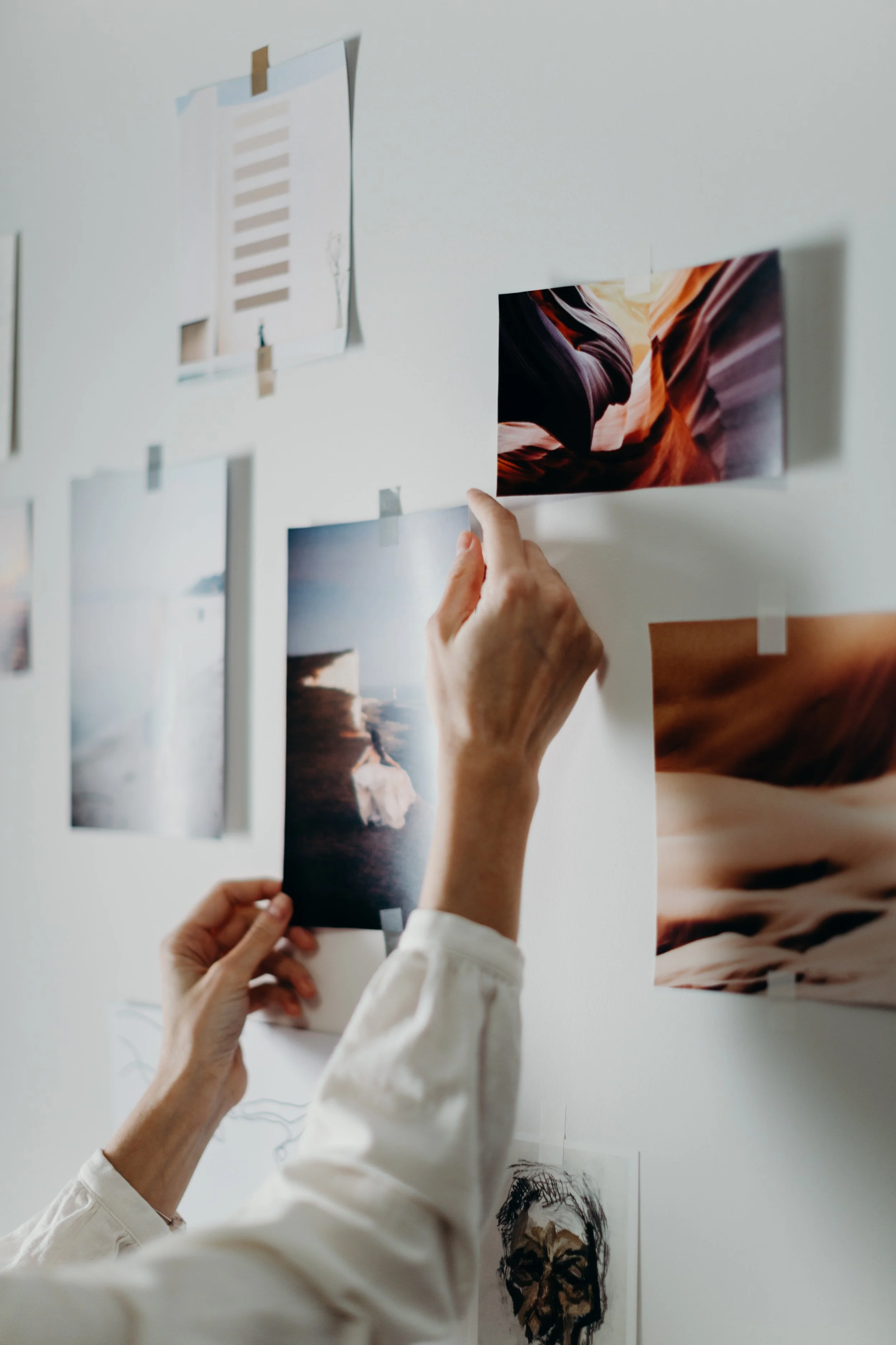 People hanging photographs on a white wall, including landscape and portrait images.