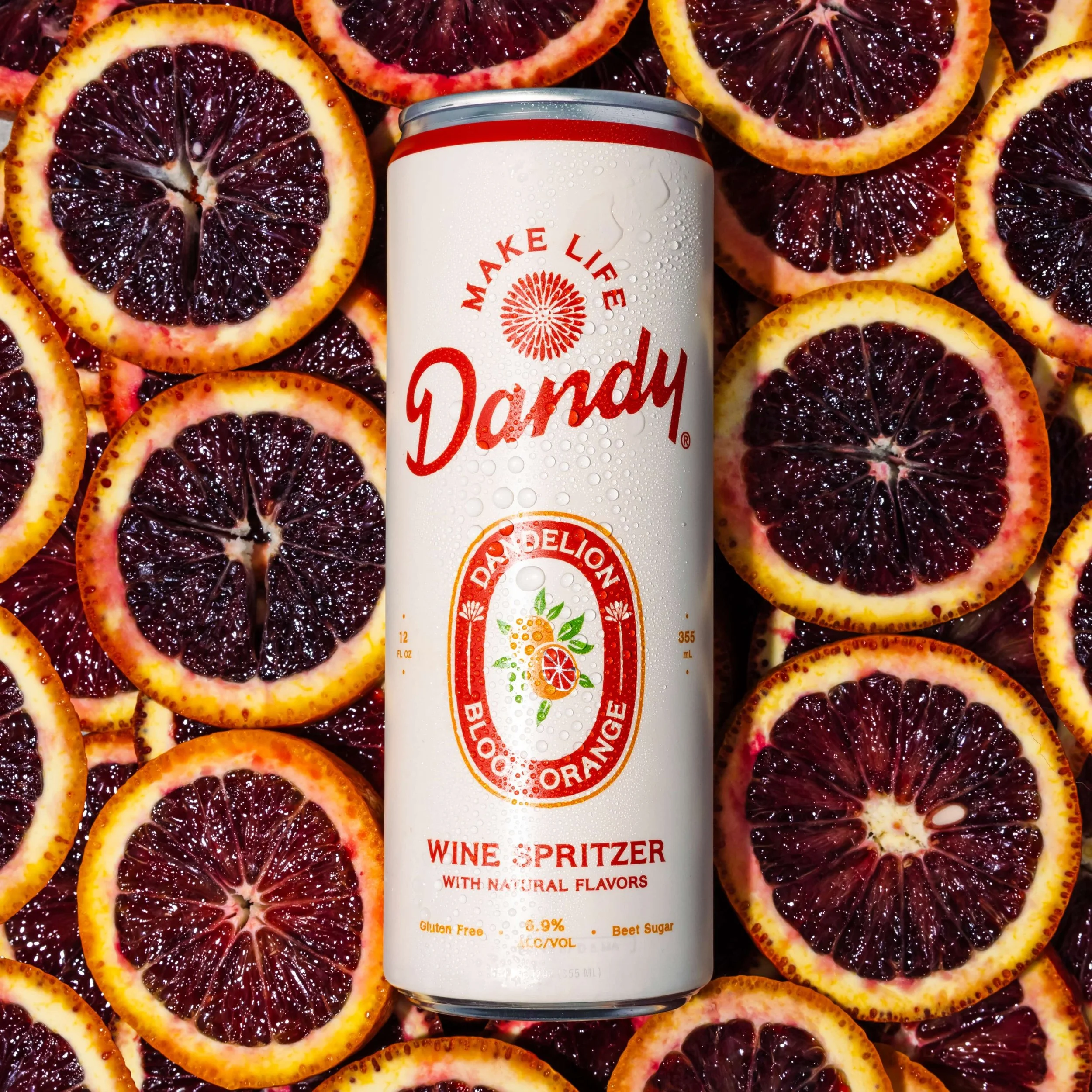 A can of wine spritzer surrounded by sliced blood oranges with dark red and orange peels.