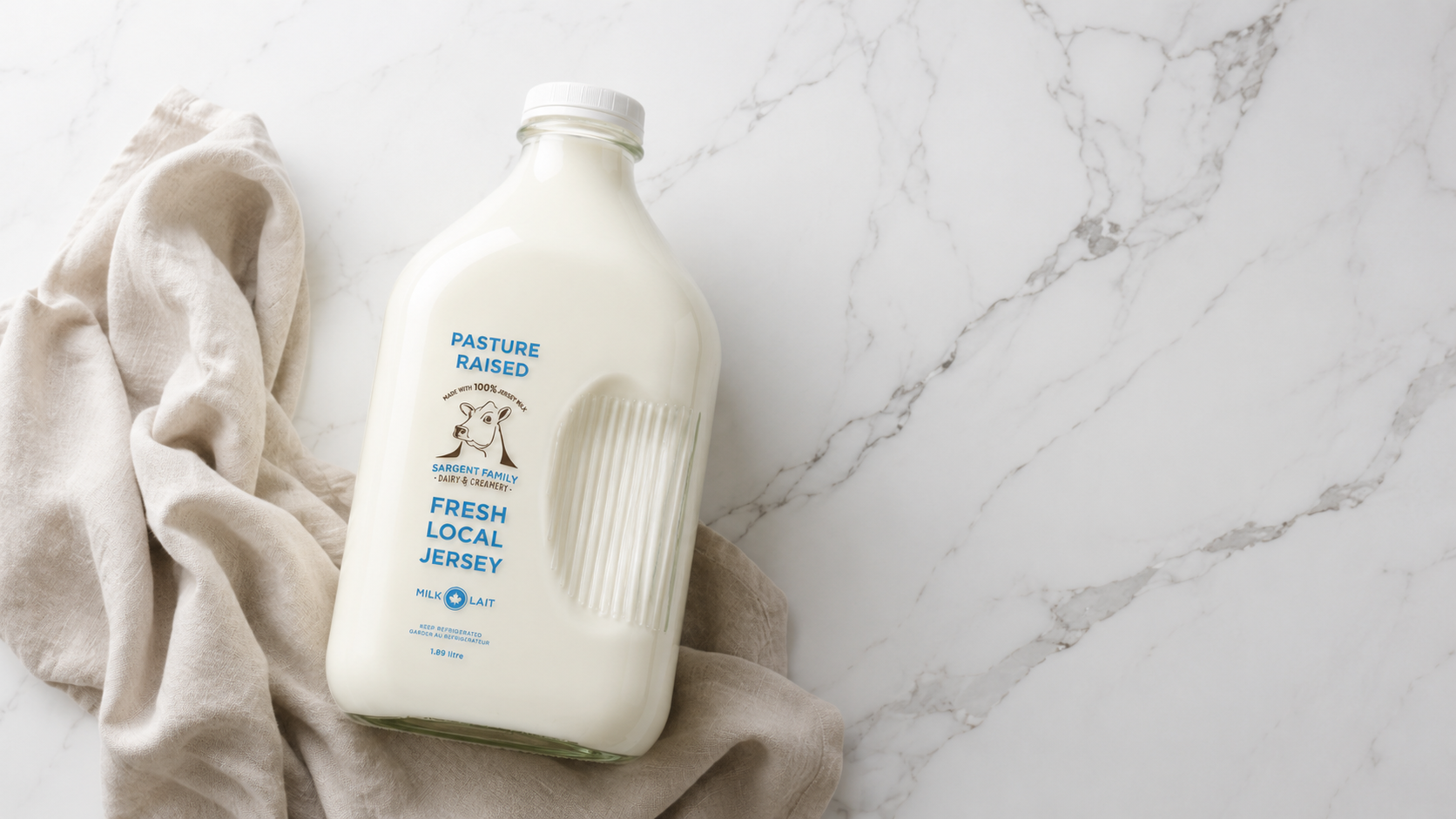 A bottle of fresh local Jersey milk on a beige cloth, on a white marble surface.