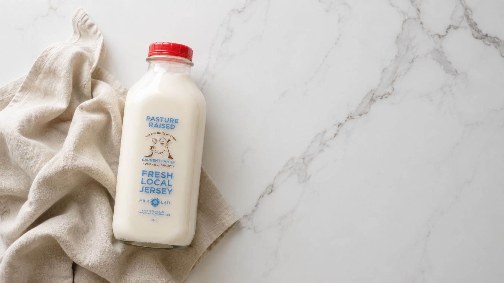 A bottle of fresh local Jersey milk placed on a beige cloth on a white marble surface.