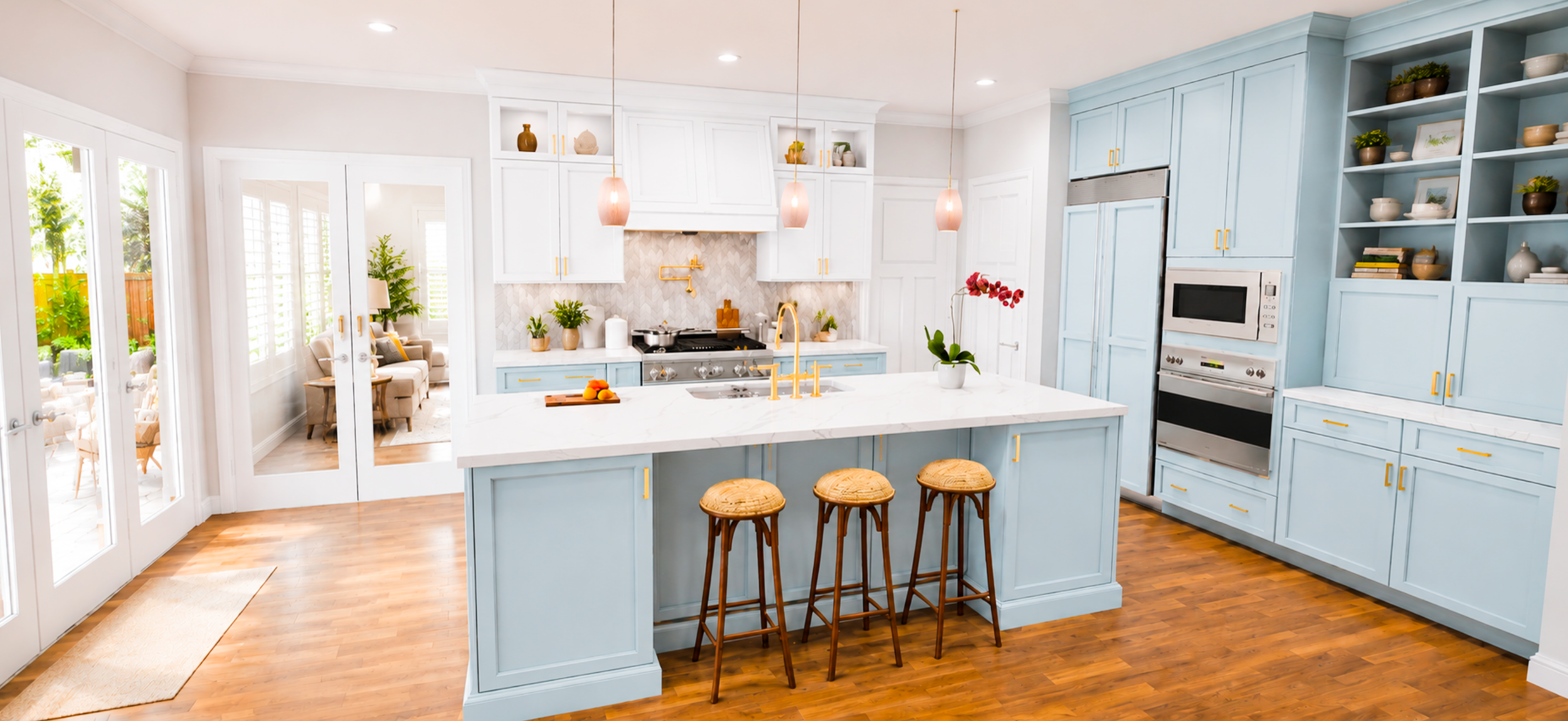 Bright kitchen with light blue cabinets, a white marble island, and wooden stools, adjacent to a living area with chairs and plants.