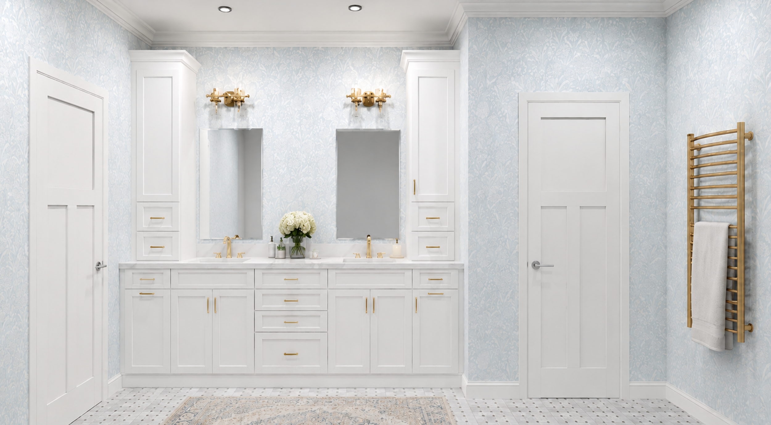 A bright modern bathroom with white cabinetry, gold fixtures, a double mirror, and light blue wallpaper with a floral pattern. There are two gold wall sconces above the mirrors, a vase of white flowers on the counter, and a wooden towel rack on the r