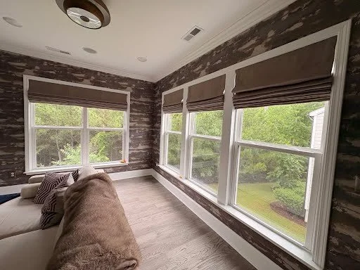 Bright sunlit room with large windows and a beige sectional sofa, overlooking a green yard.