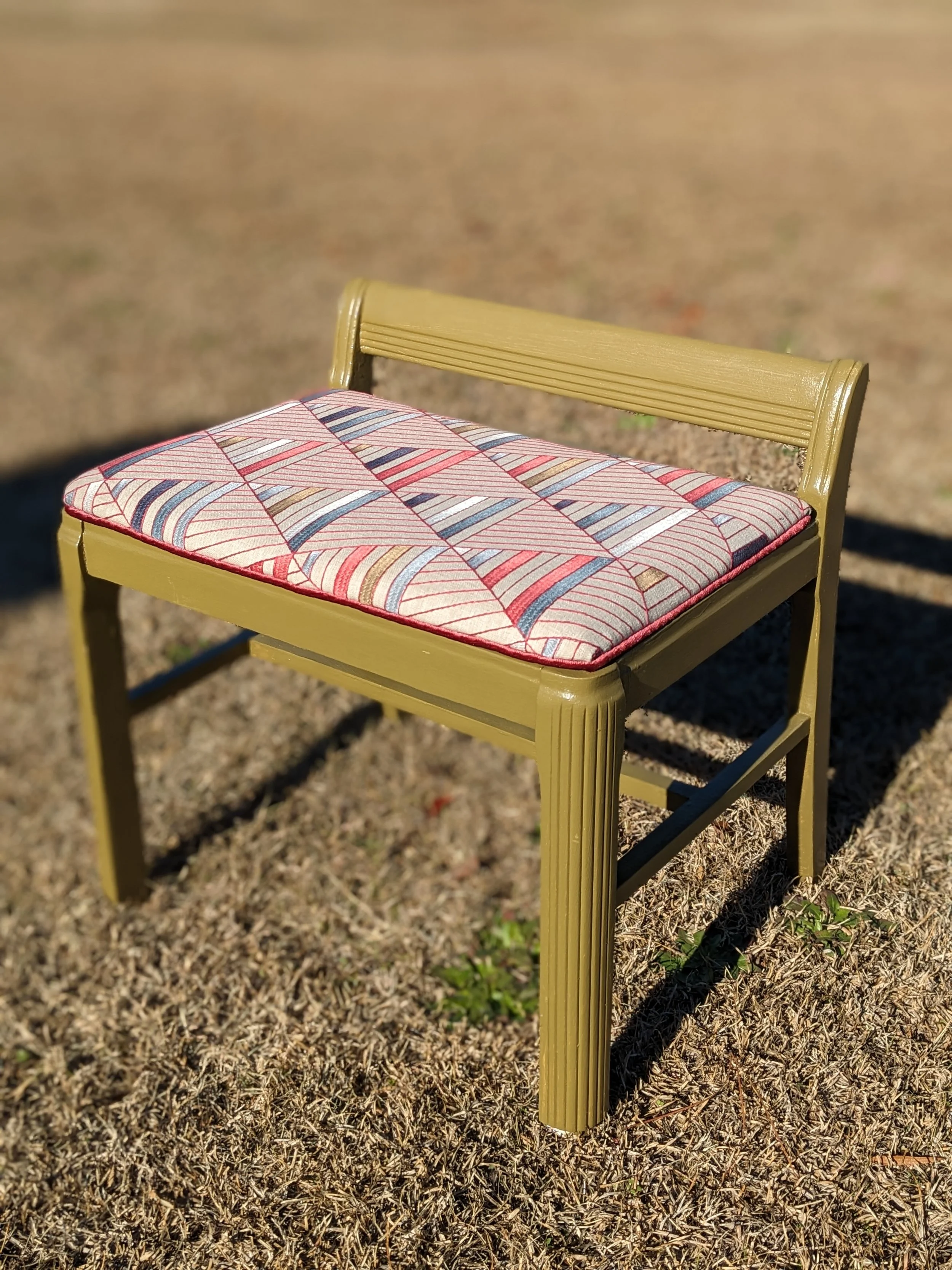 A yellow chair with a patterned cushioned seat on a grassy outdoor area.