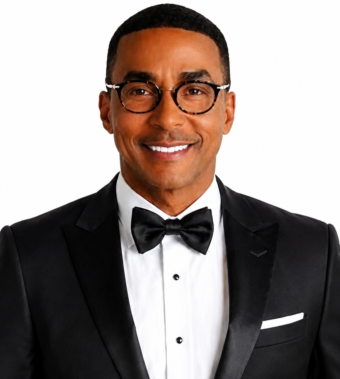 A man smiling while wearing a black tuxedo with a bow tie and glasses.
