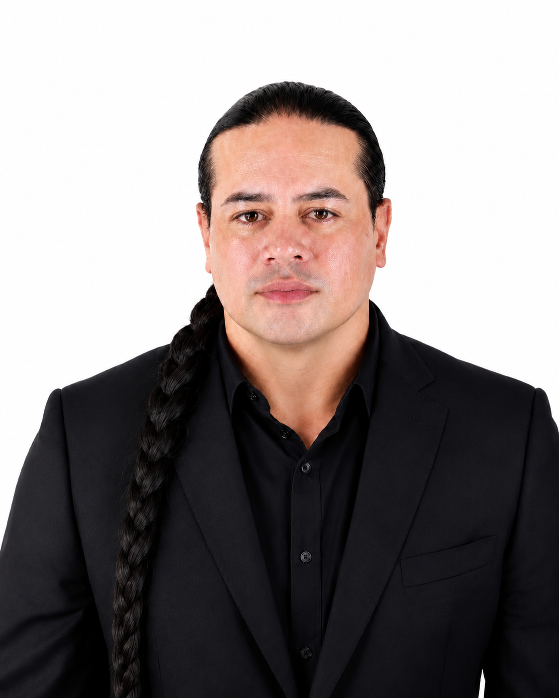 A man with long black hair in a braid, wearing a black suit and black shirt, looking directly at the camera against a white background.
