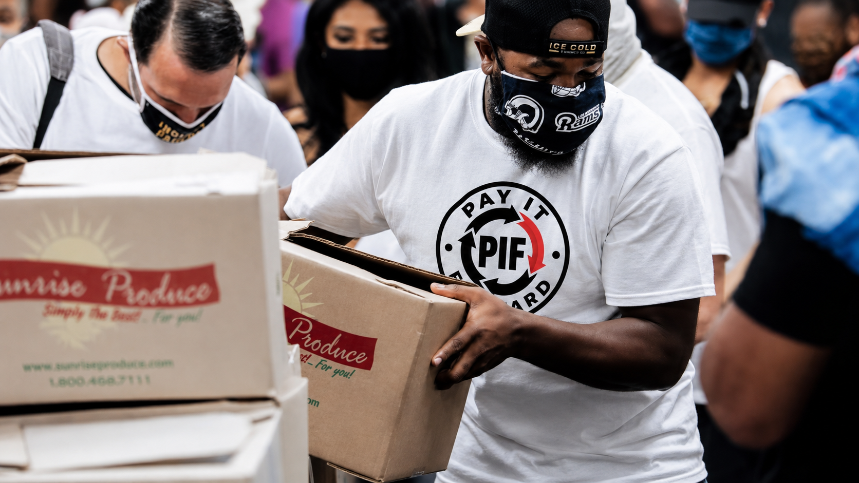 People wearing masks and t-shirts, unloading boxes at a food distribution event.