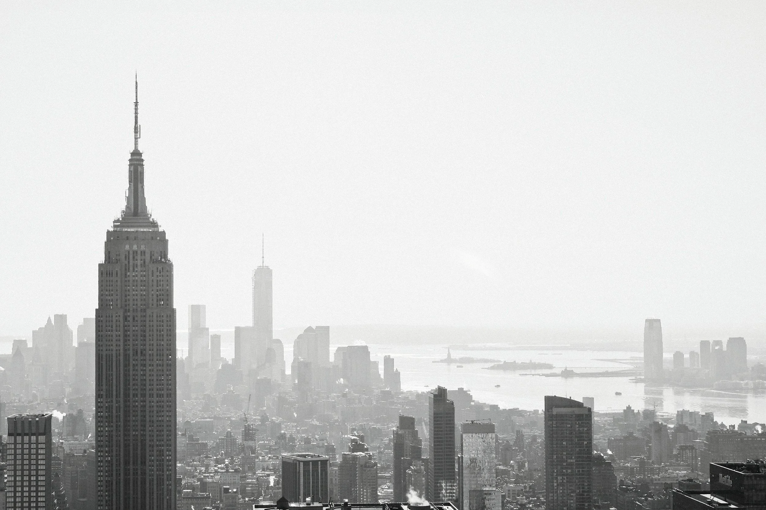 A black and white photo of the New York City skyline featuring the Empire State Building in the foreground and One World Trade Center in the background.