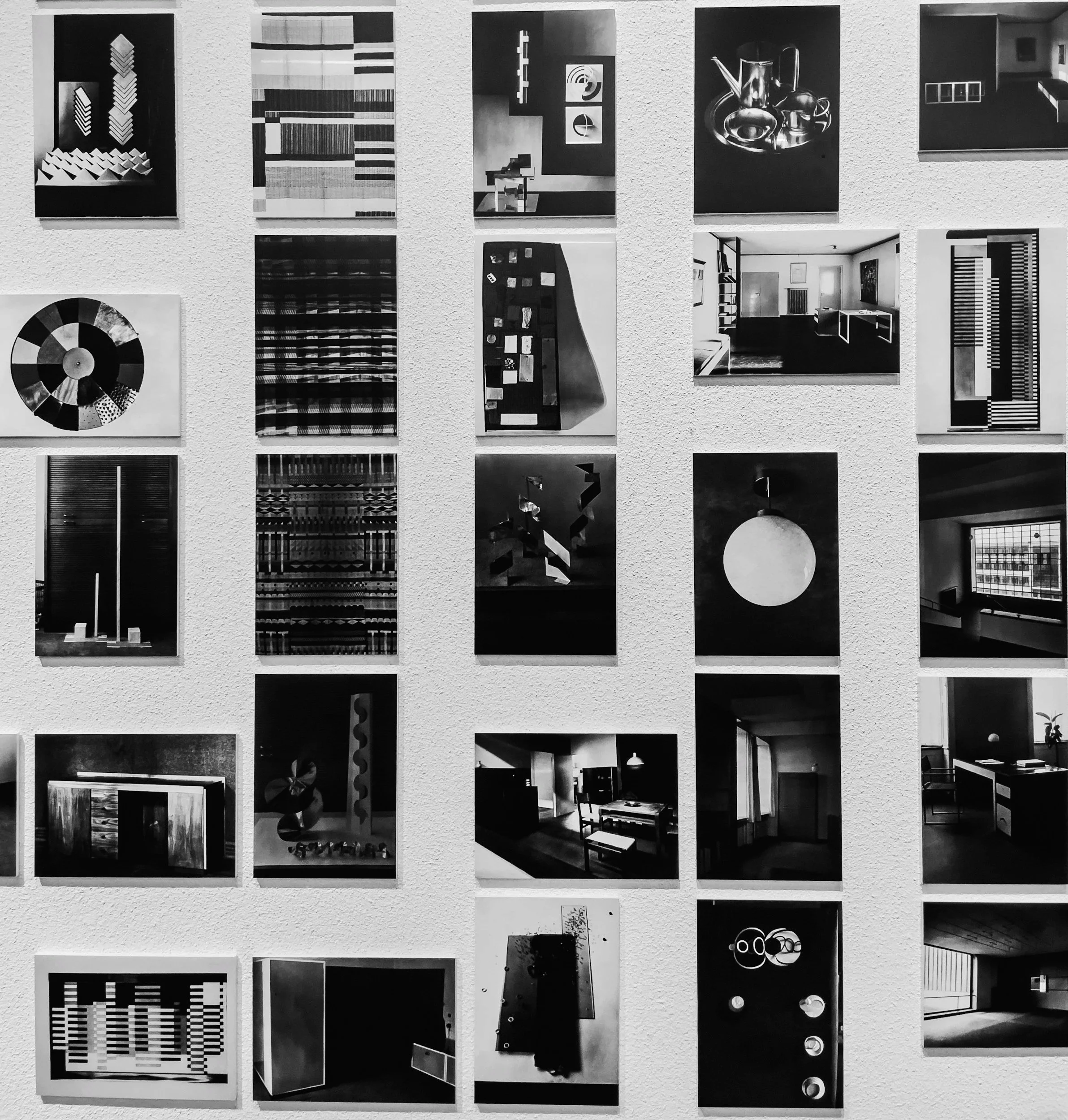Collection of black-and-white photographs showcasing various modern and abstract interior design elements, including furniture, architectural details, and artistic objects displayed on a white textured wall.