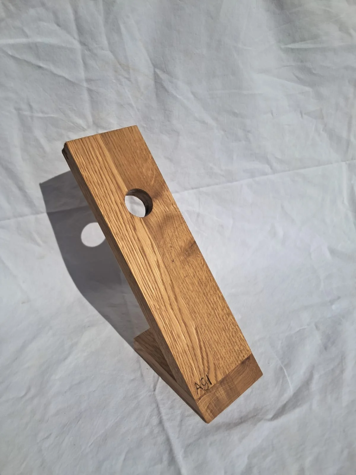 Ein rechteckiges Stück Holz mit zwei runden Löchern, auf weißem, leicht verknittertem Hintergrund.