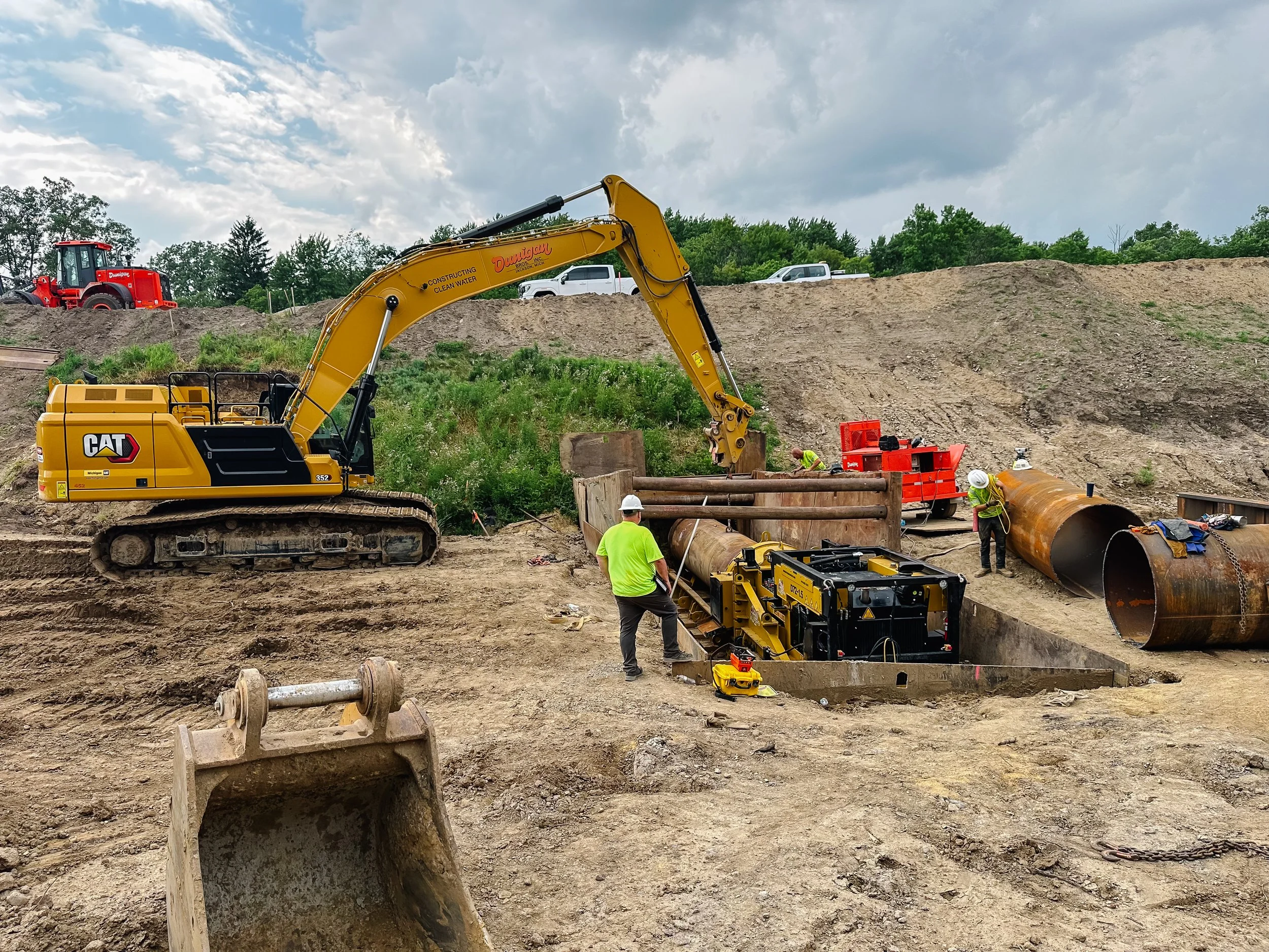 Dunigan Bros. excavator, crew members, and large diameter pipe on an active underground utility project