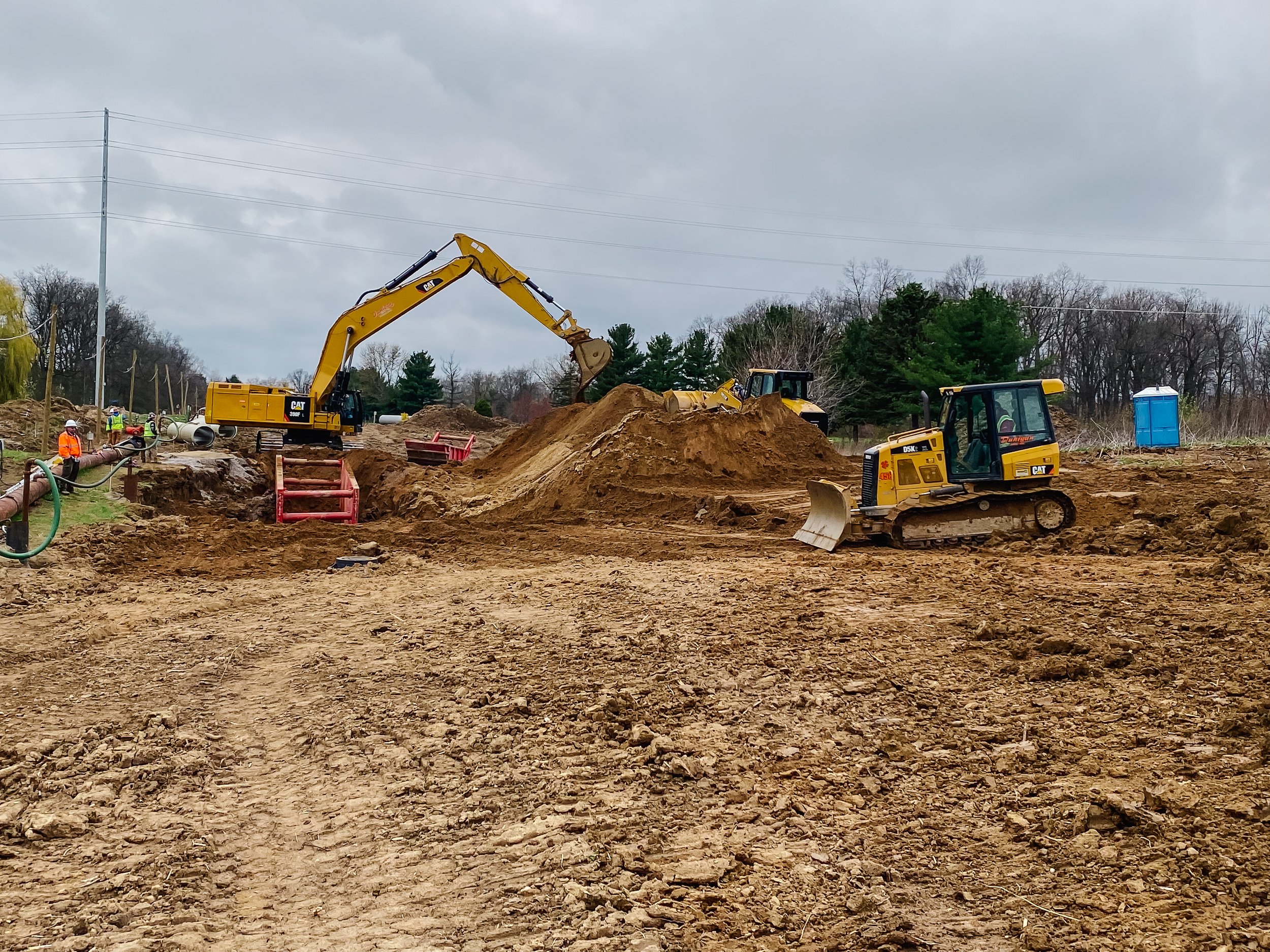 Dunigan Bros. excavator and crew members on an underground utility project with pipe on the ground
