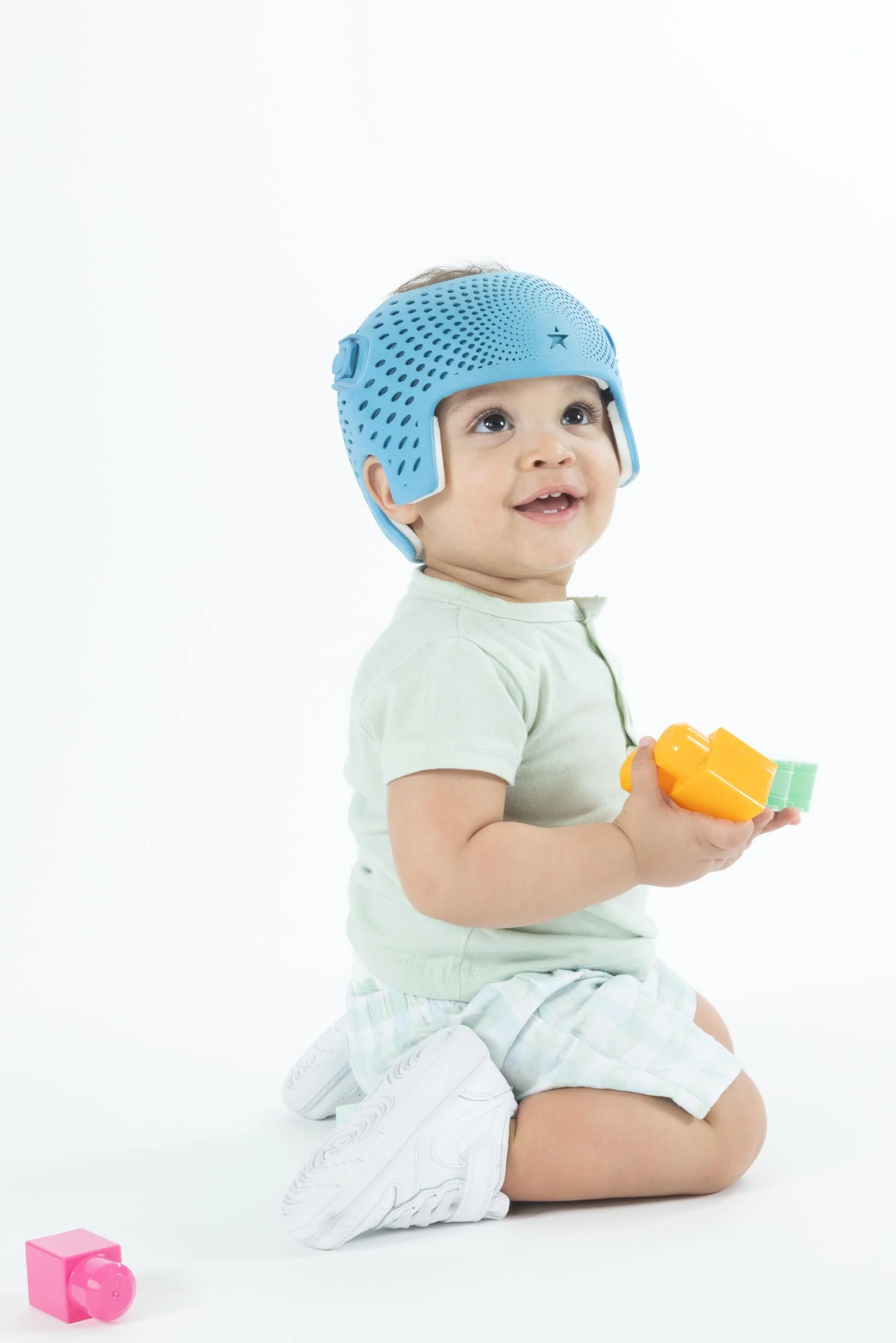A young child playing with a block while kneeling and wearing a blue 3D cranial remolding helmet.
