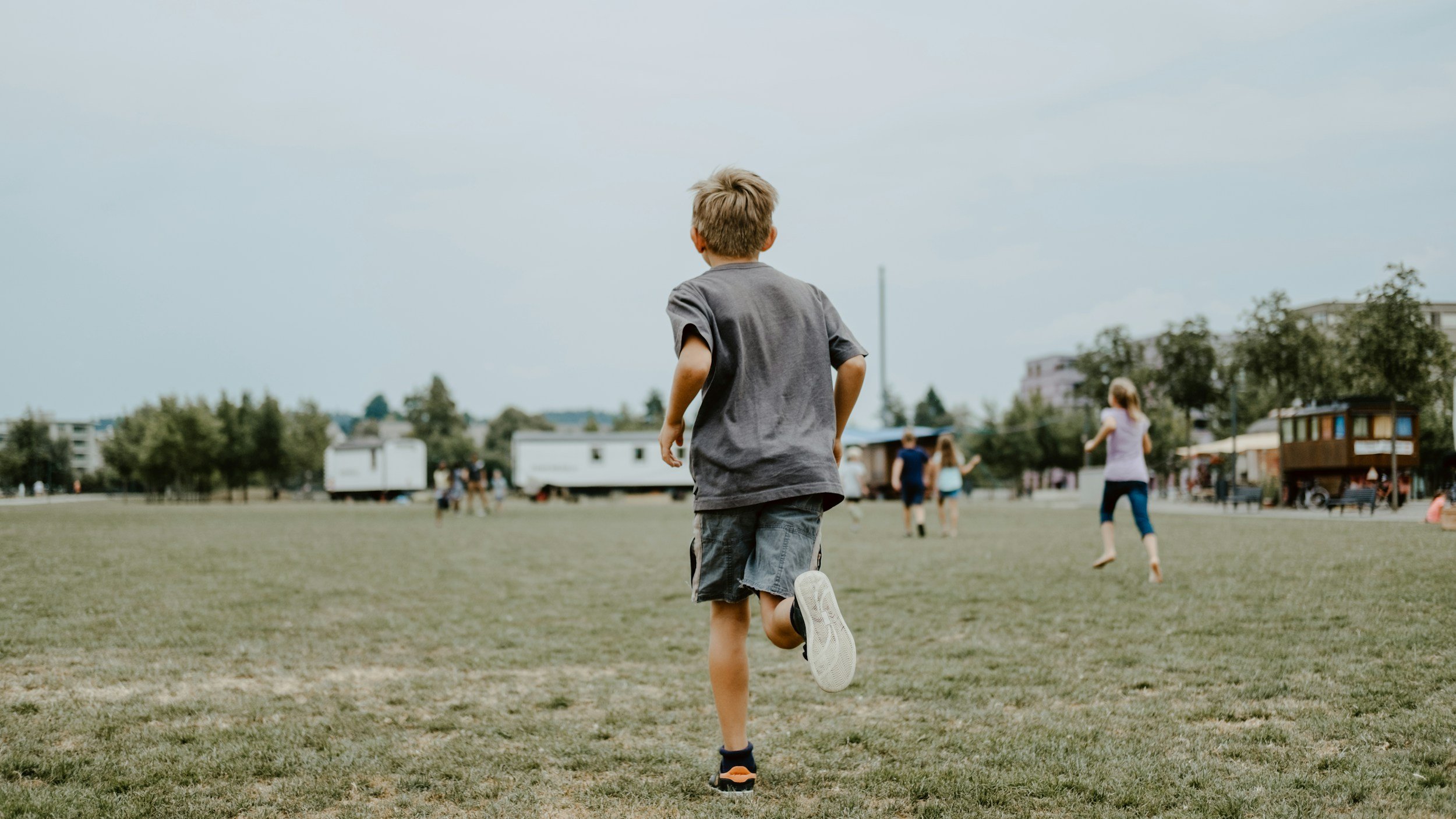 Boy running on a grassy field with other children playing in the background.