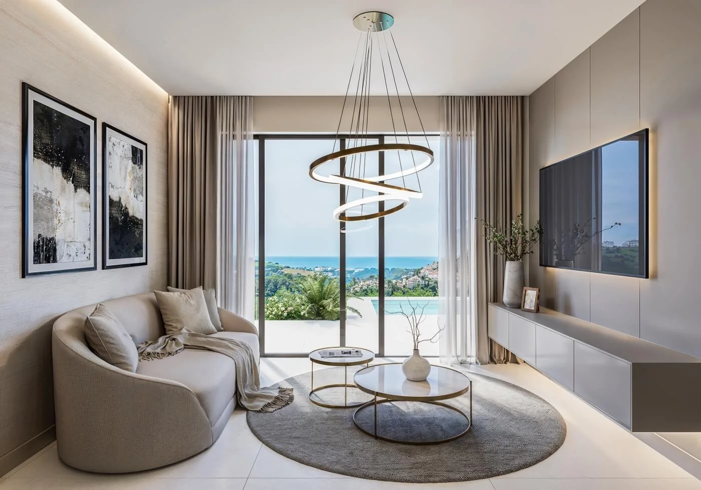 Modern living room with beige curved sofa, abstract black and white artwork, round coffee tables with a white vase, large window with sheer curtains, view of greenery and ocean outside, chandelier, flat-screen TV, and a floating console with vases and picture frame.