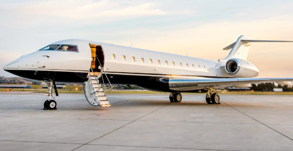 Private jet parked on tarmac with stairs extended for boarding, under a partly cloudy sky.