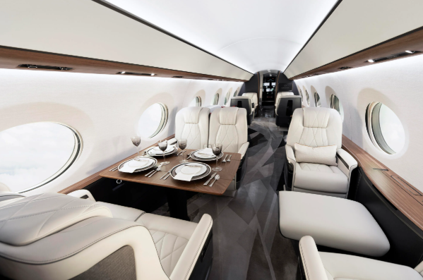 Luxury private jet interior with a dining table set with plates, glasses, and silverware, and beige leather seats along the windows.