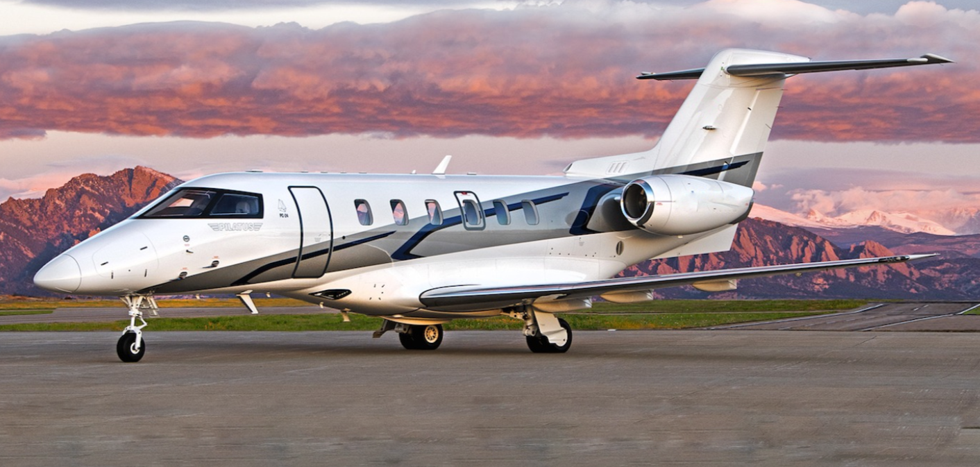 A white private jet airplane parked on a runway at sunset with mountains in the background.