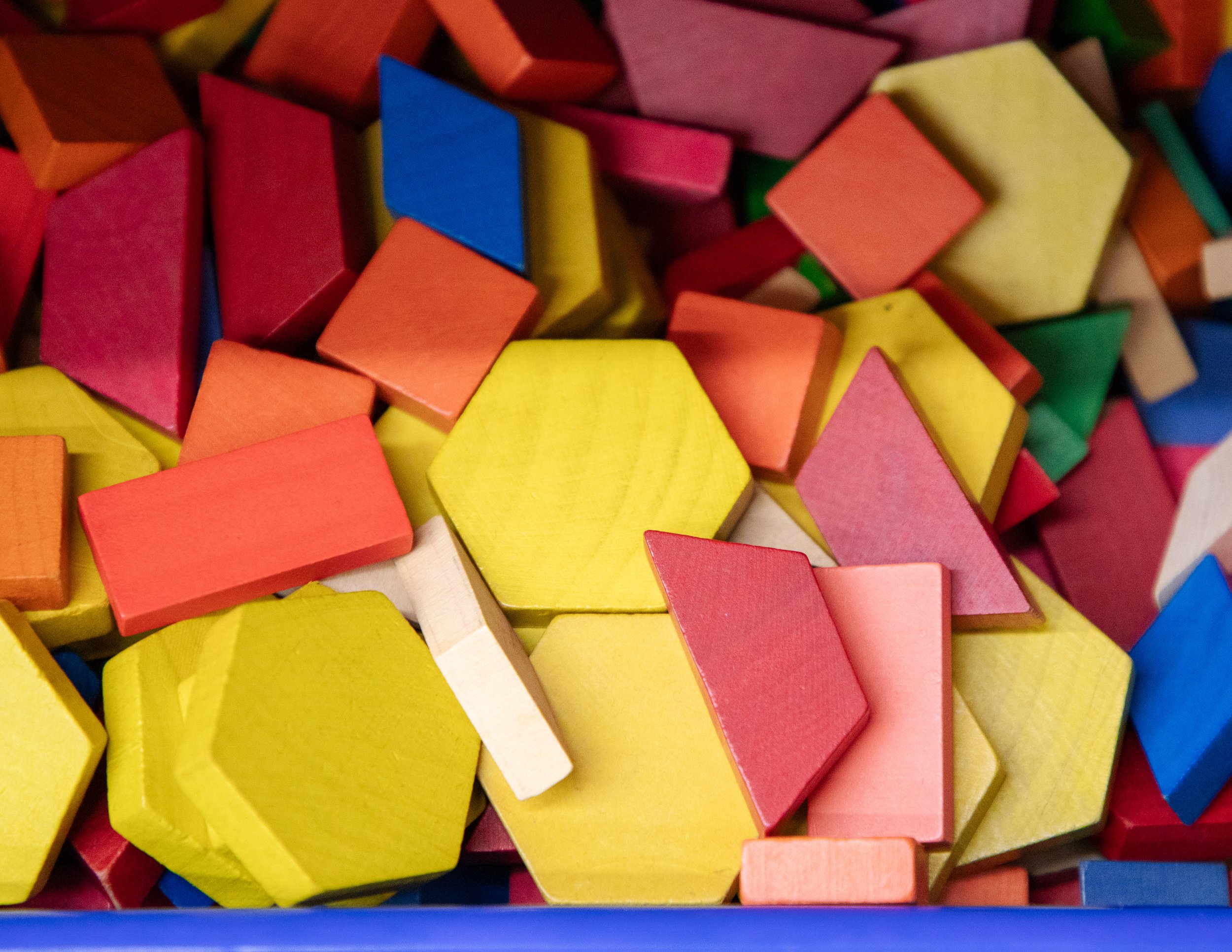 Close-up of colorful wooden building blocks in various shapes, including squares, triangles, and rectangles, in bright colors like yellow, pink, blue, green, orange, and red.