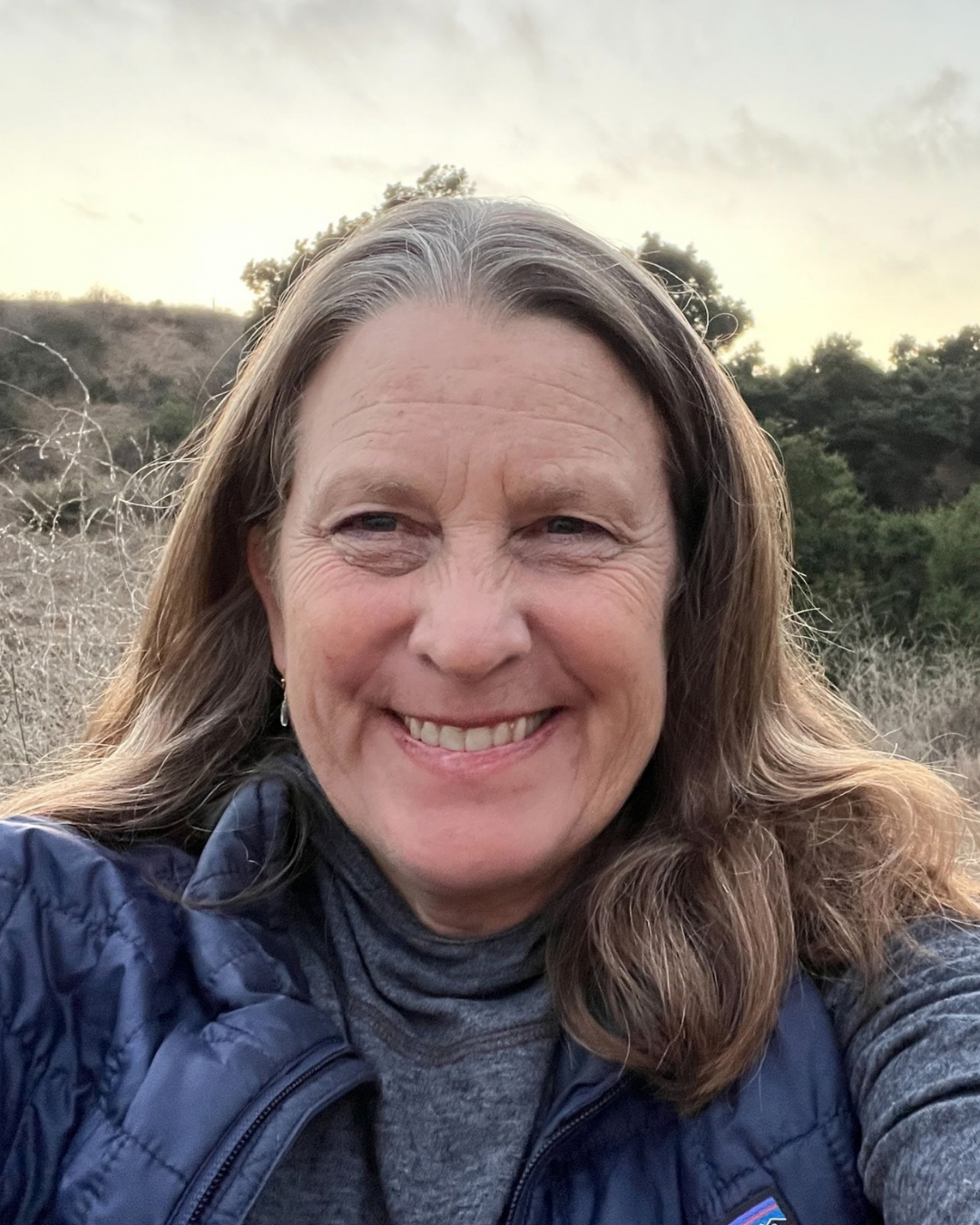 A woman wearing a sweater and jacket in an outdoor setting.