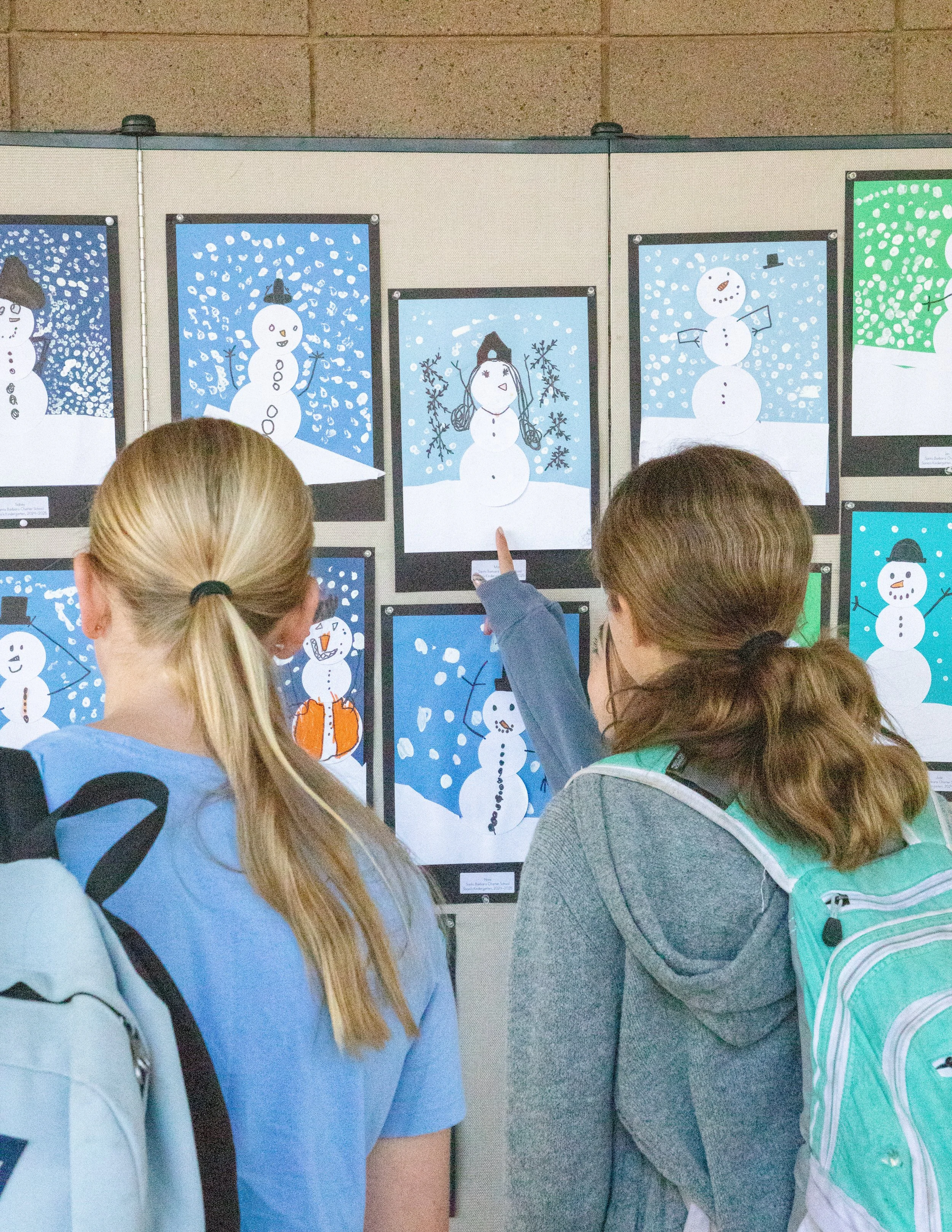 Children looking at a display of snowman artwork on a wall.