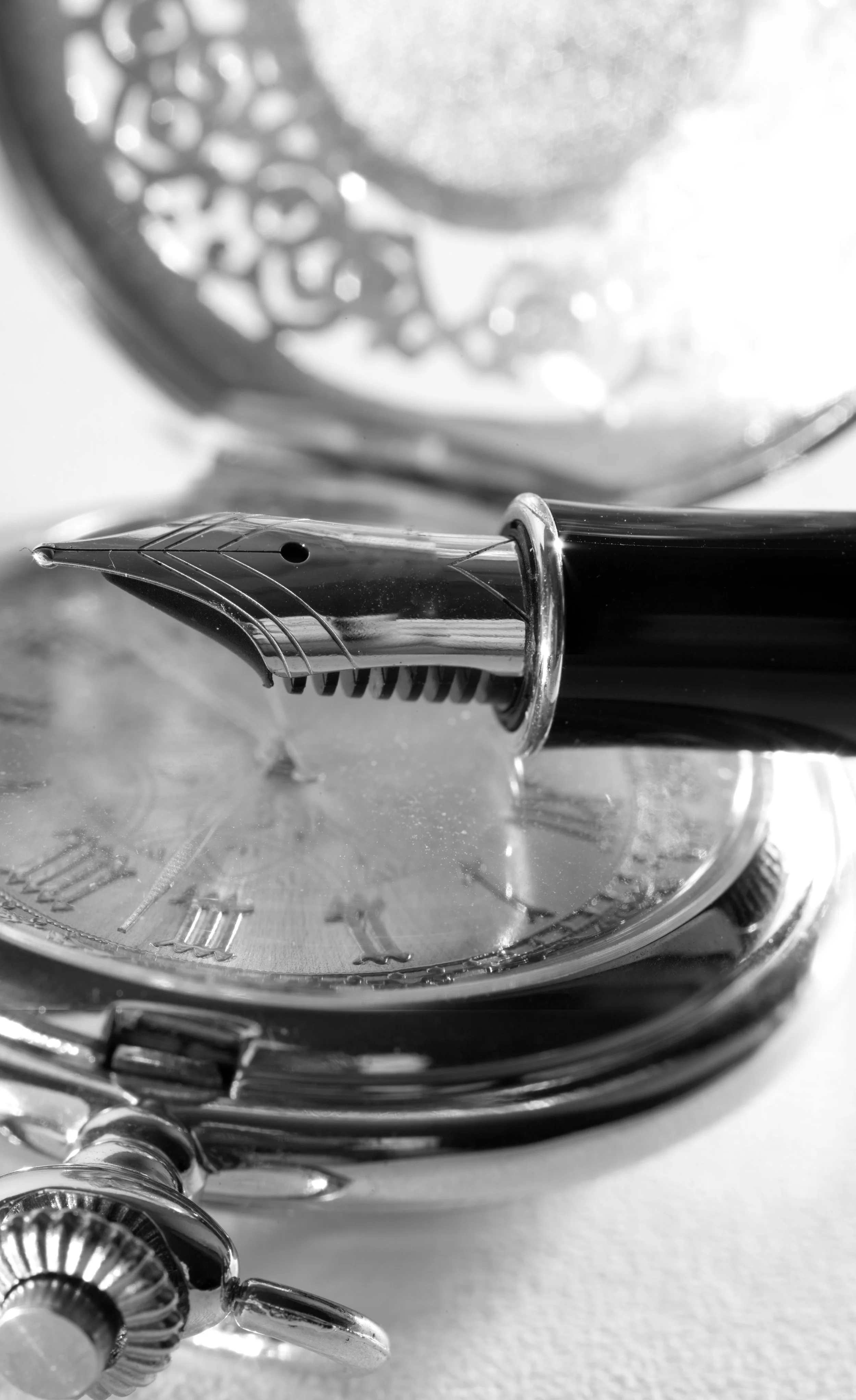 Close-up of a fountain pen resting on a watch with a metallic band and a clear face showing Roman numerals.
