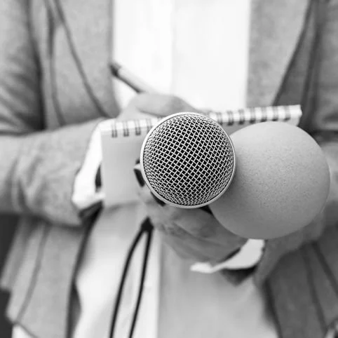 Close-up of a person holding a microphone and a notepad with a pen, image in black and white.