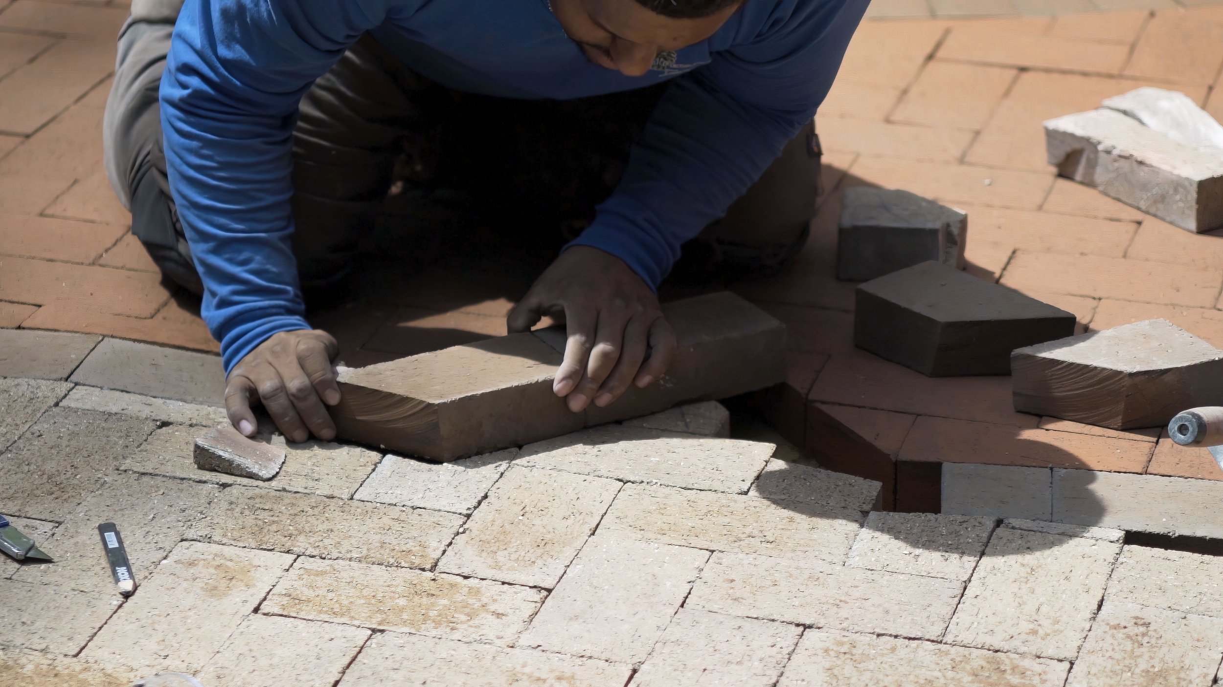 A person installing bricks on a sidewalk, kneeling down and placing bricks in a pattern.