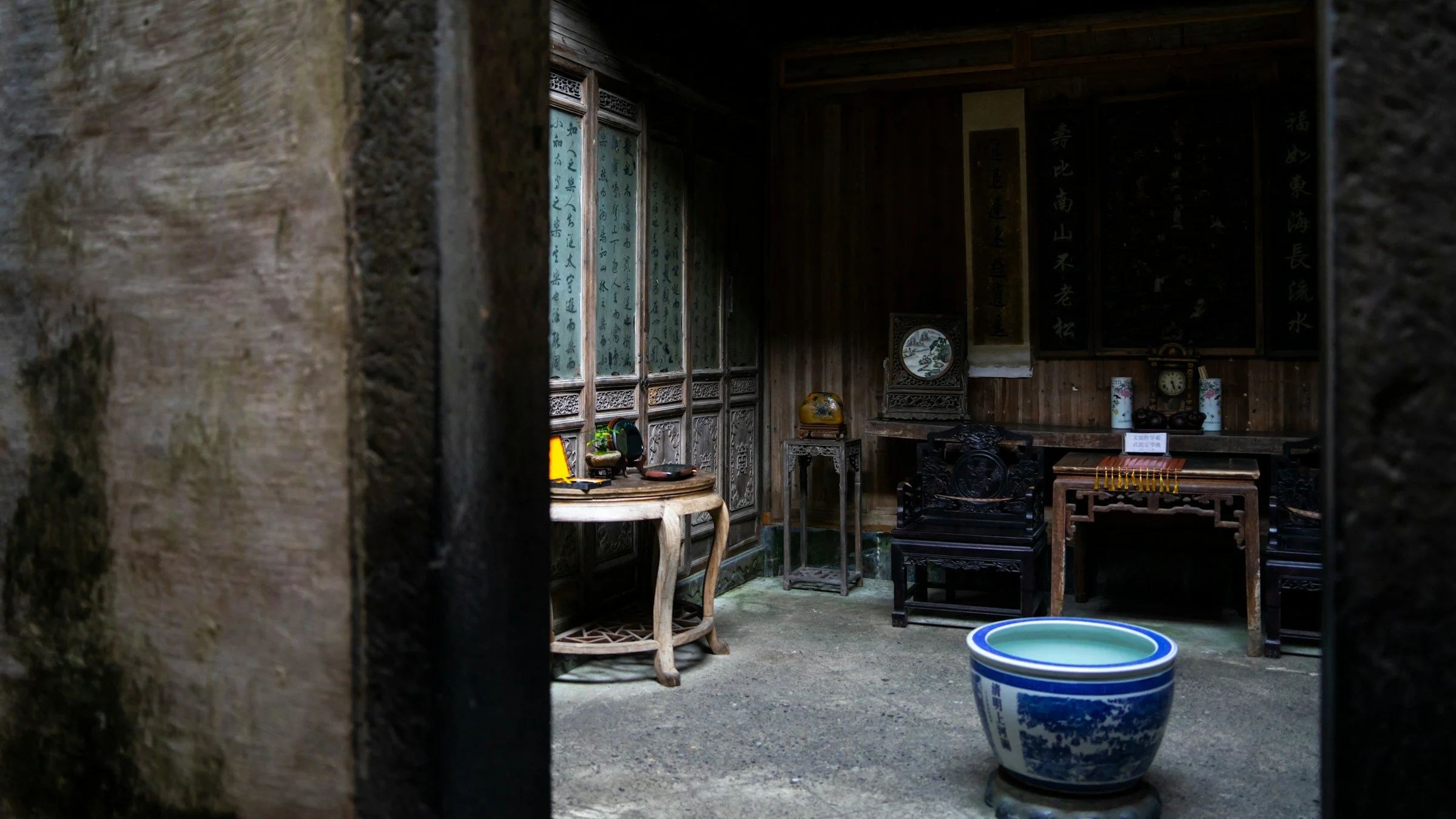 View of traditional Chinese interior decor with wooden furniture, calligraphy wall hangings, and ceramic vases.