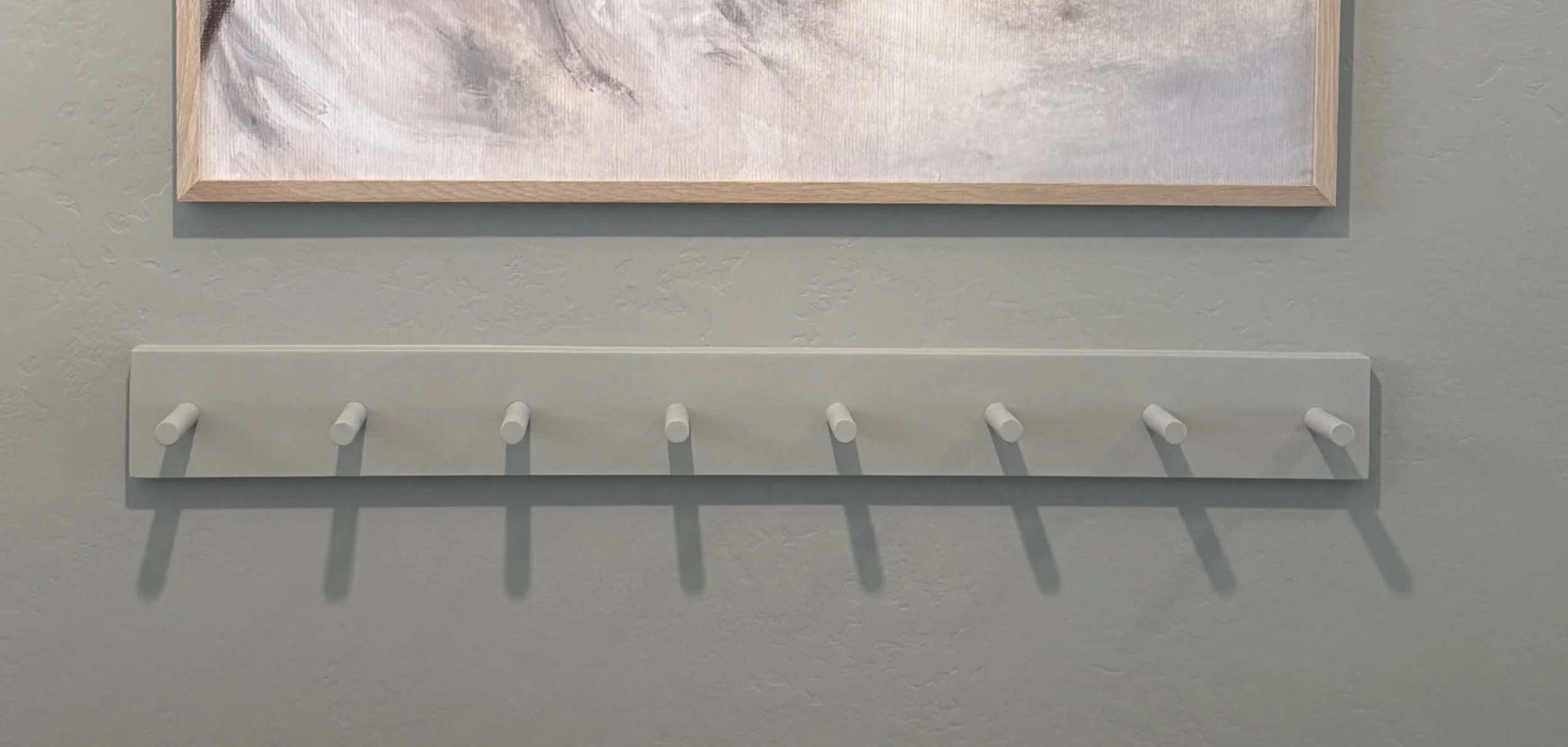 Front view of a custom wall-mounted wood peg rack with eight pegs painted to blend with the wall.