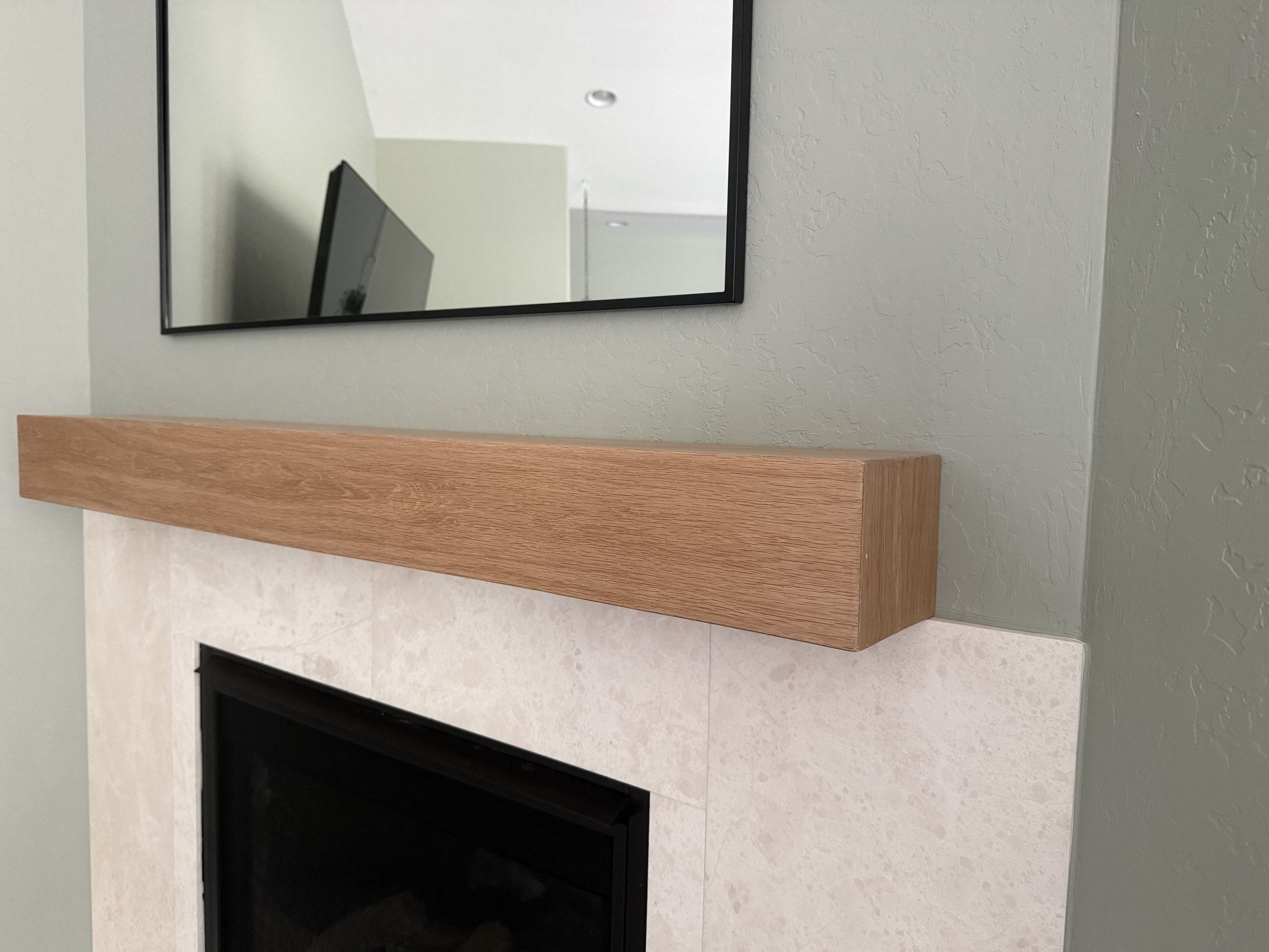 Custom white oak mantel installed above a marble tile fireplace surround