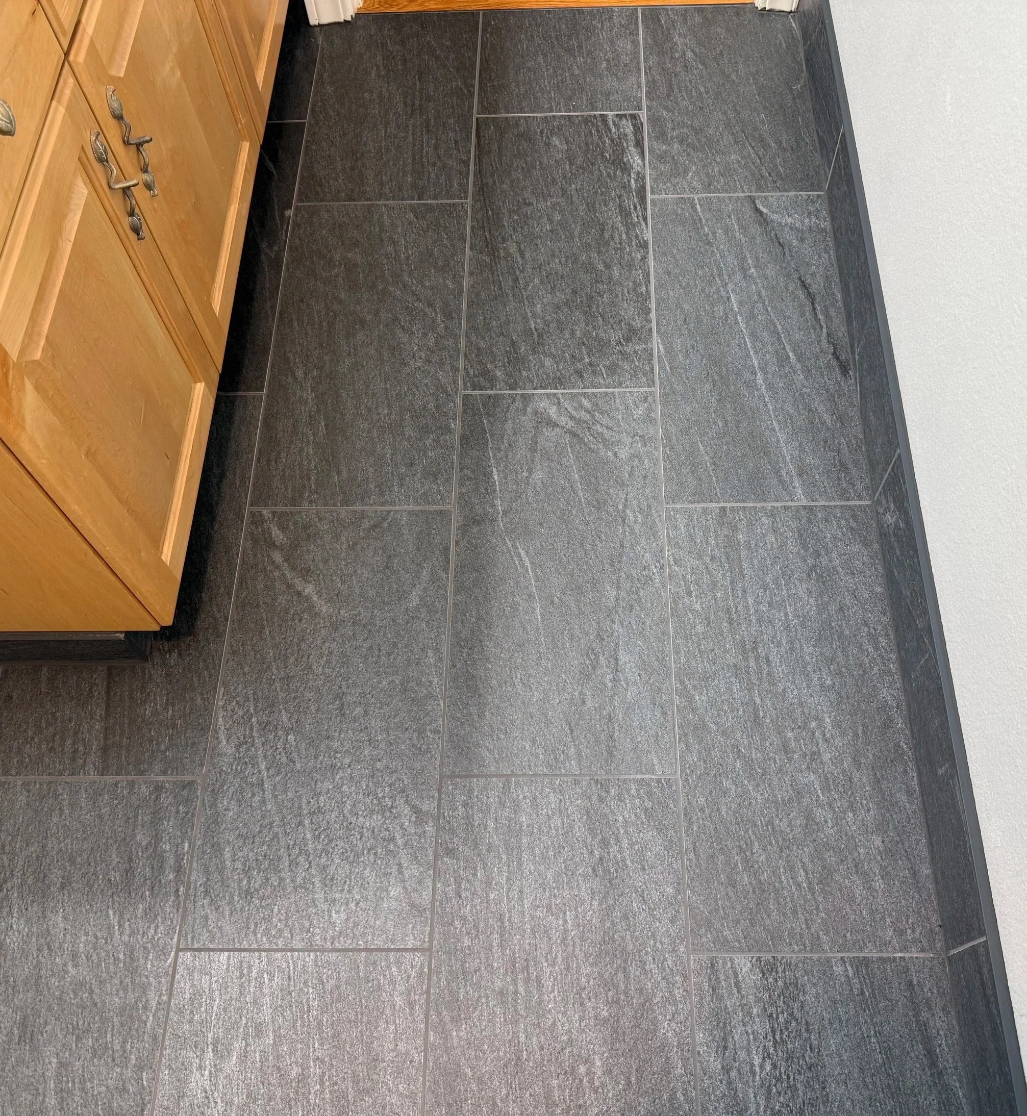 Close-up of large-format charcoal porcelain floor tile with coordinating tiled baseboard.