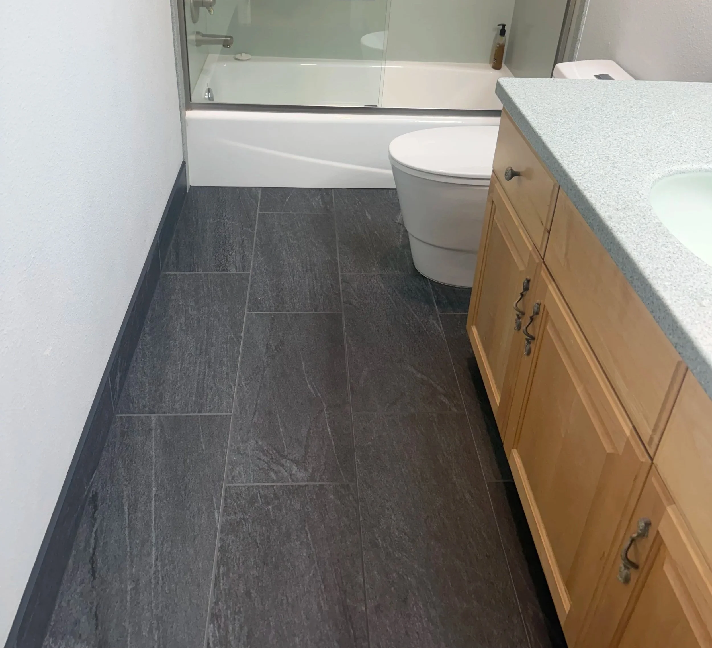 Bathroom with large-format charcoal porcelain tile flooring and coordinating tiled baseboards