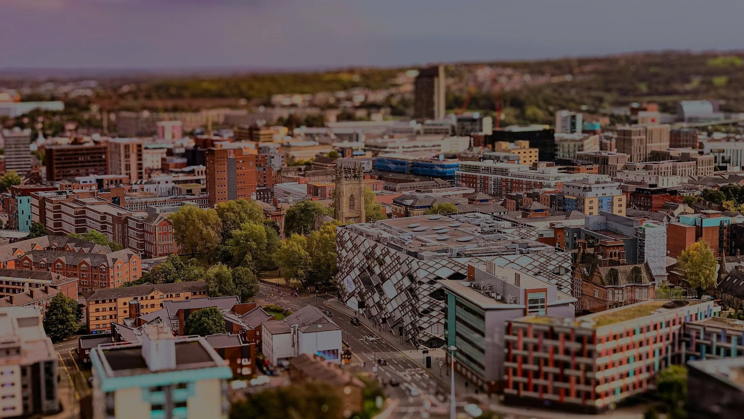 Aerial view of a Sheffield cityscape with various buildings, trees, and a church with a tall steeple.