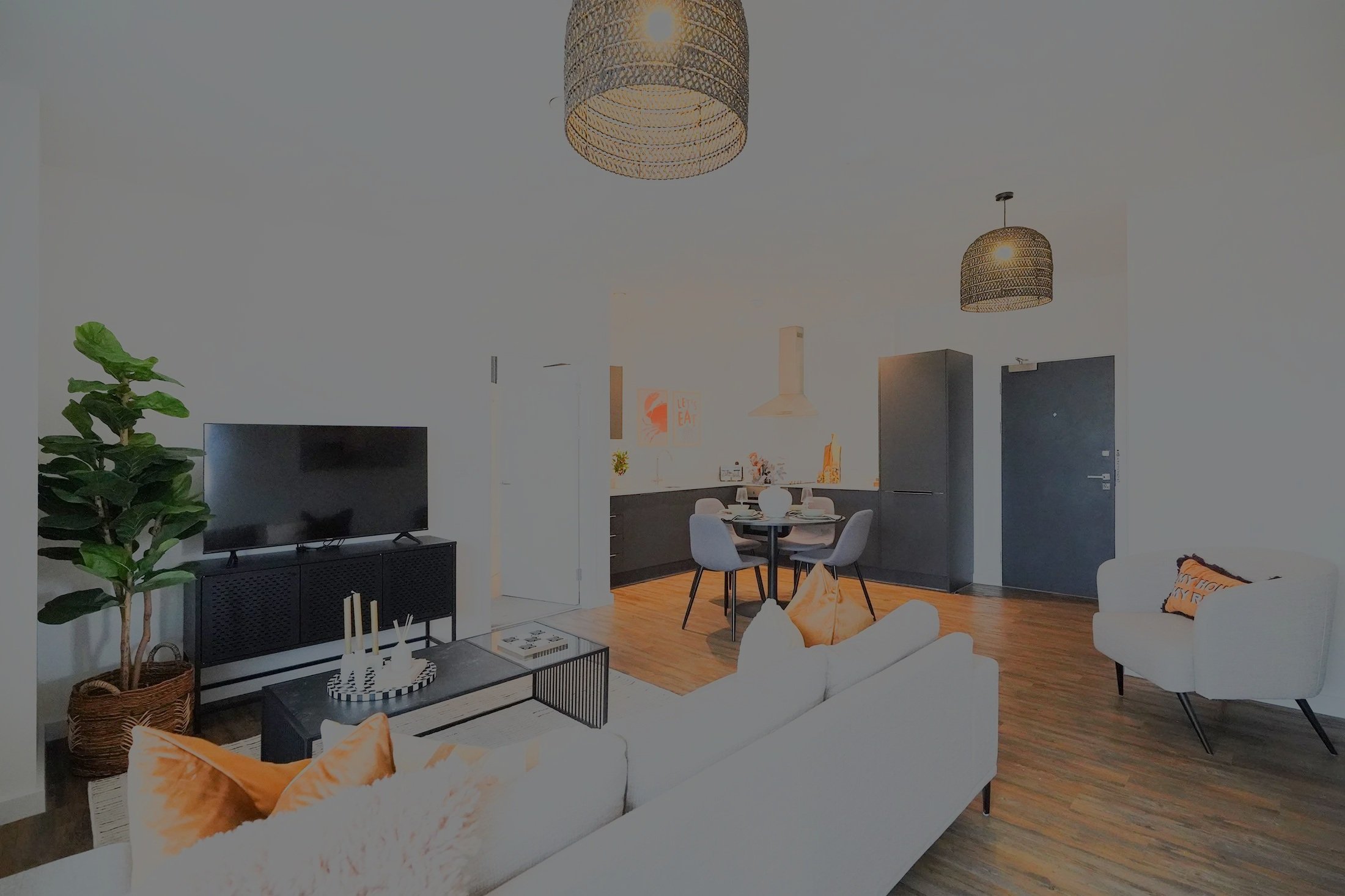 Modern living room with white sofa, orange cushions, black coffee table, TV on black stand, potted plant, hanging woven lamps, and dining area with round table and four chairs.