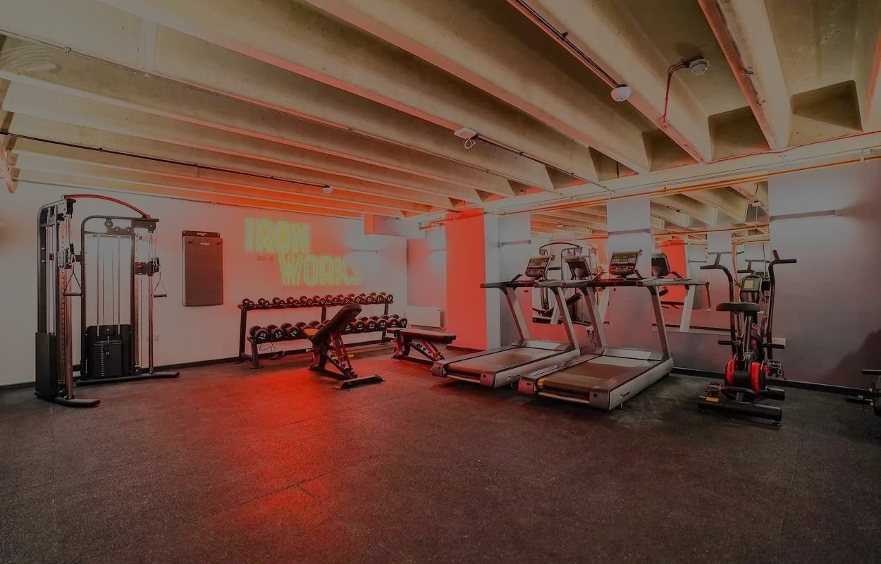 Empty gym at Iron Yard with workout equipment including treadmill, rowing machine, dumbbells, exercise bench, and cardio machines in a modern fitness center.