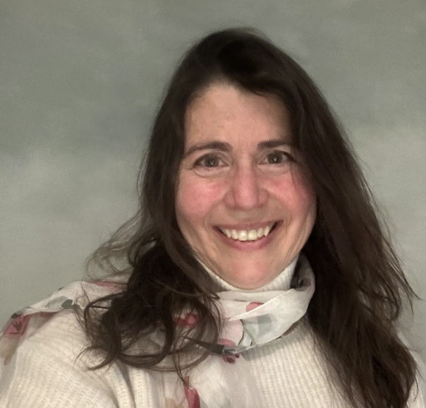 A smiling woman with long brown hair, wearing a beige sweater and a floral scarf, against a plain background.