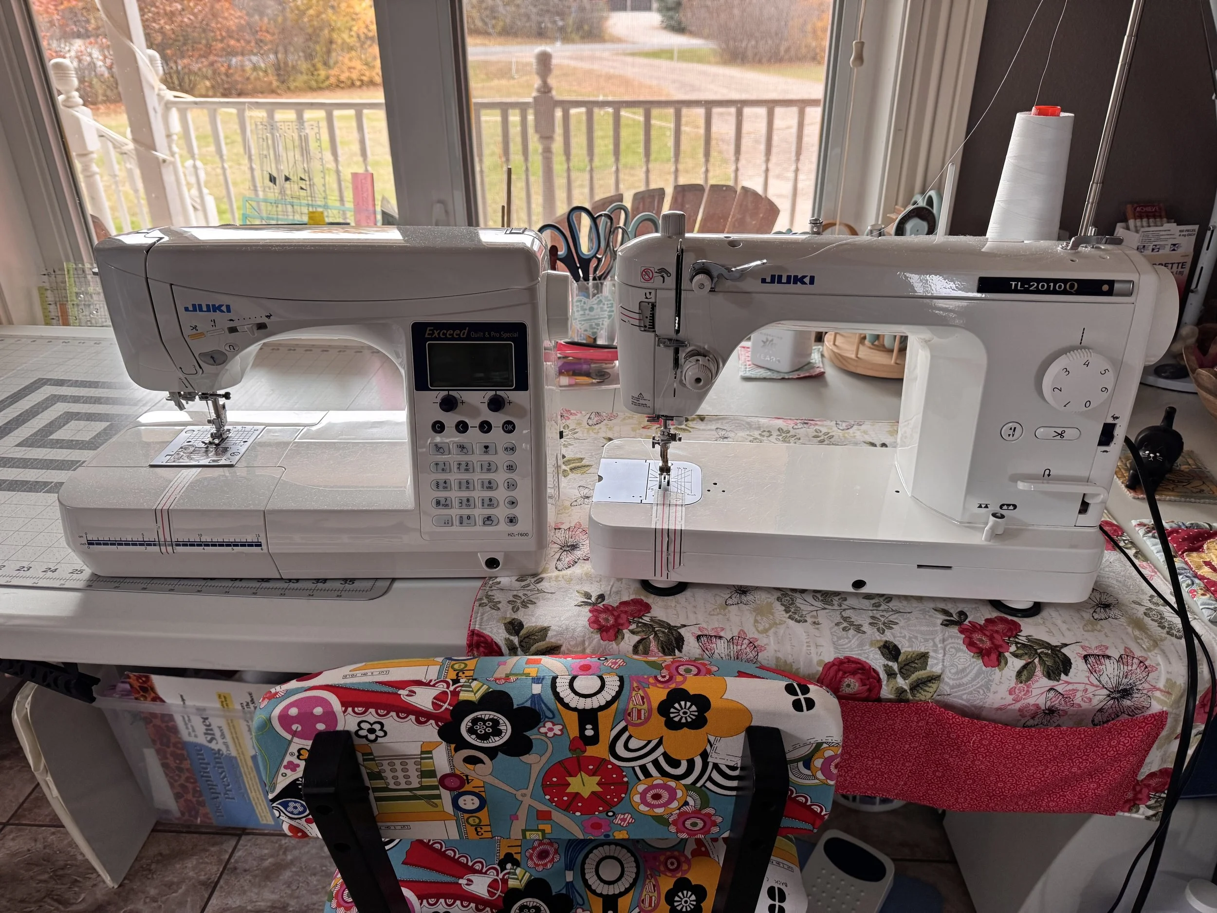 Two Juki sewing machines, including an HZL-F600 and TL-2010Q, on a sewing table with fabric and quilting supplies.