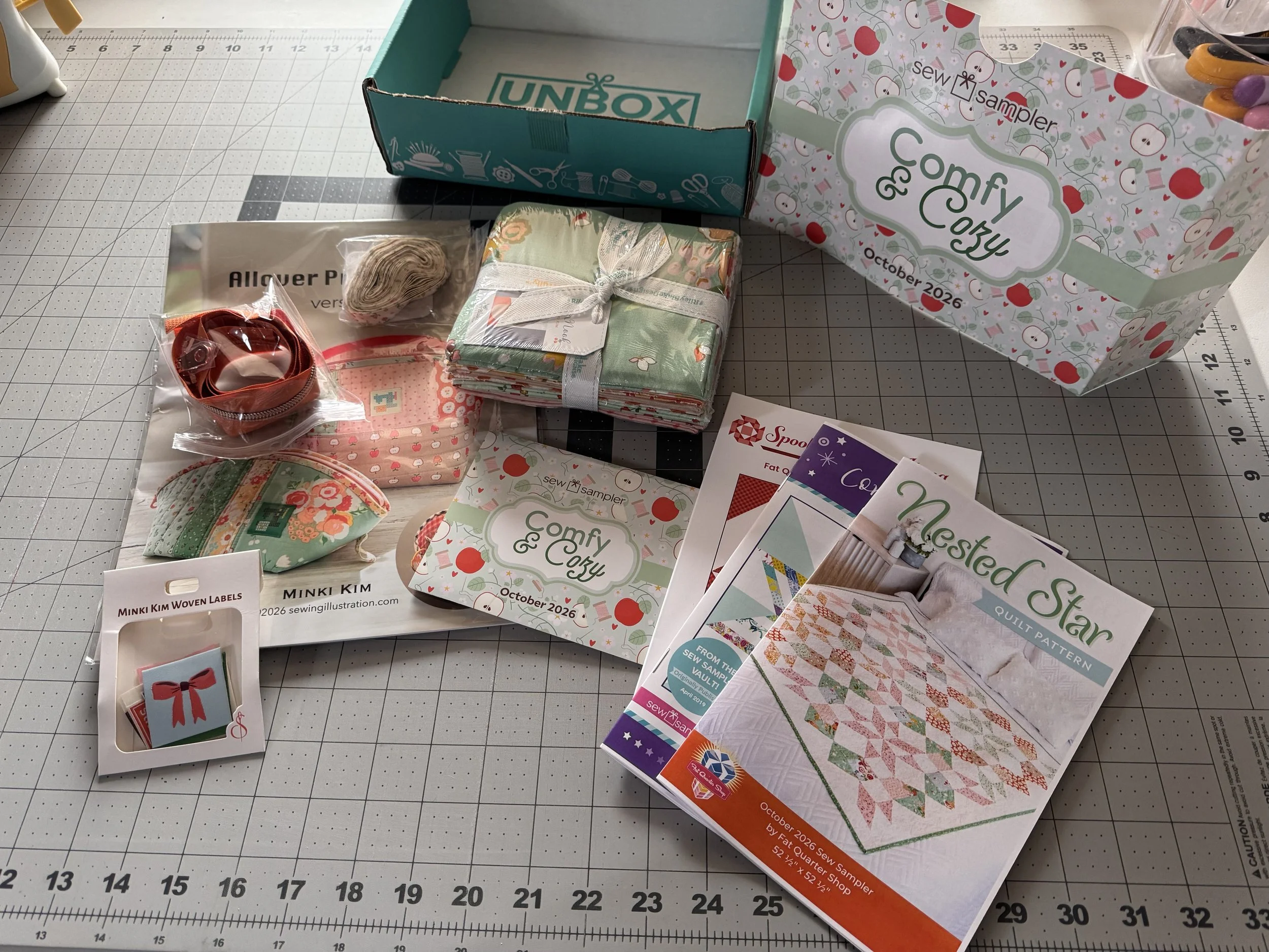 October 2026 Fat Quarter Shop Sew Sampler subscription box with quilting fabrics, patterns, and sewing notions displayed on a cutting mat
