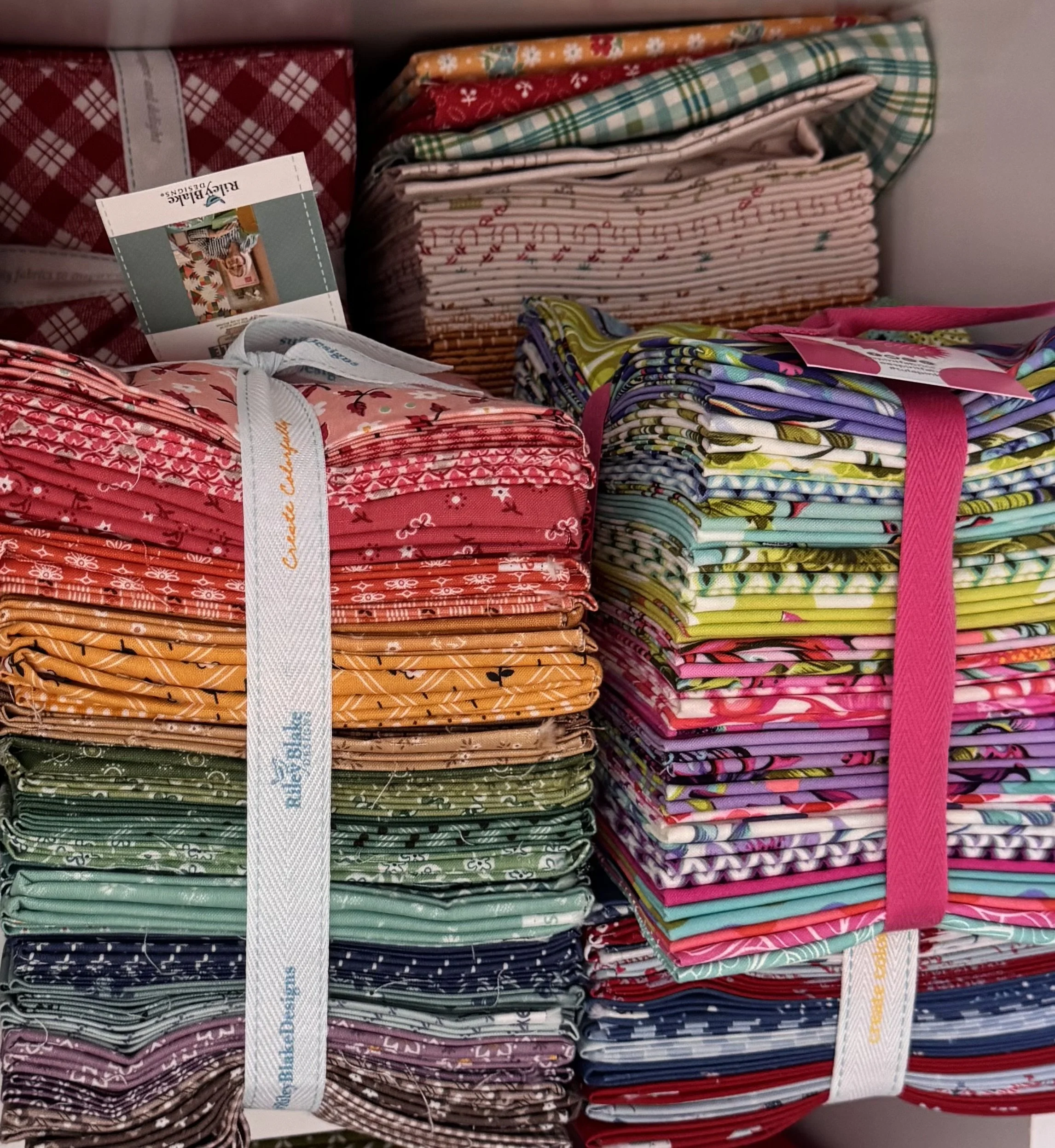 Assorted quilting cotton fabrics, precut bundles, and quilt-making supplies.