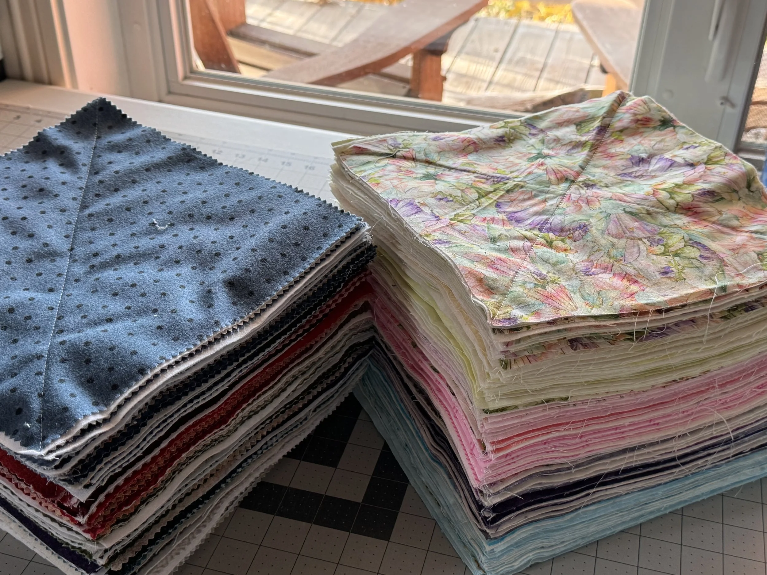Stacks of colorful handmade rag quilt squares in pastel floral and blue fabrics, ready for assembly