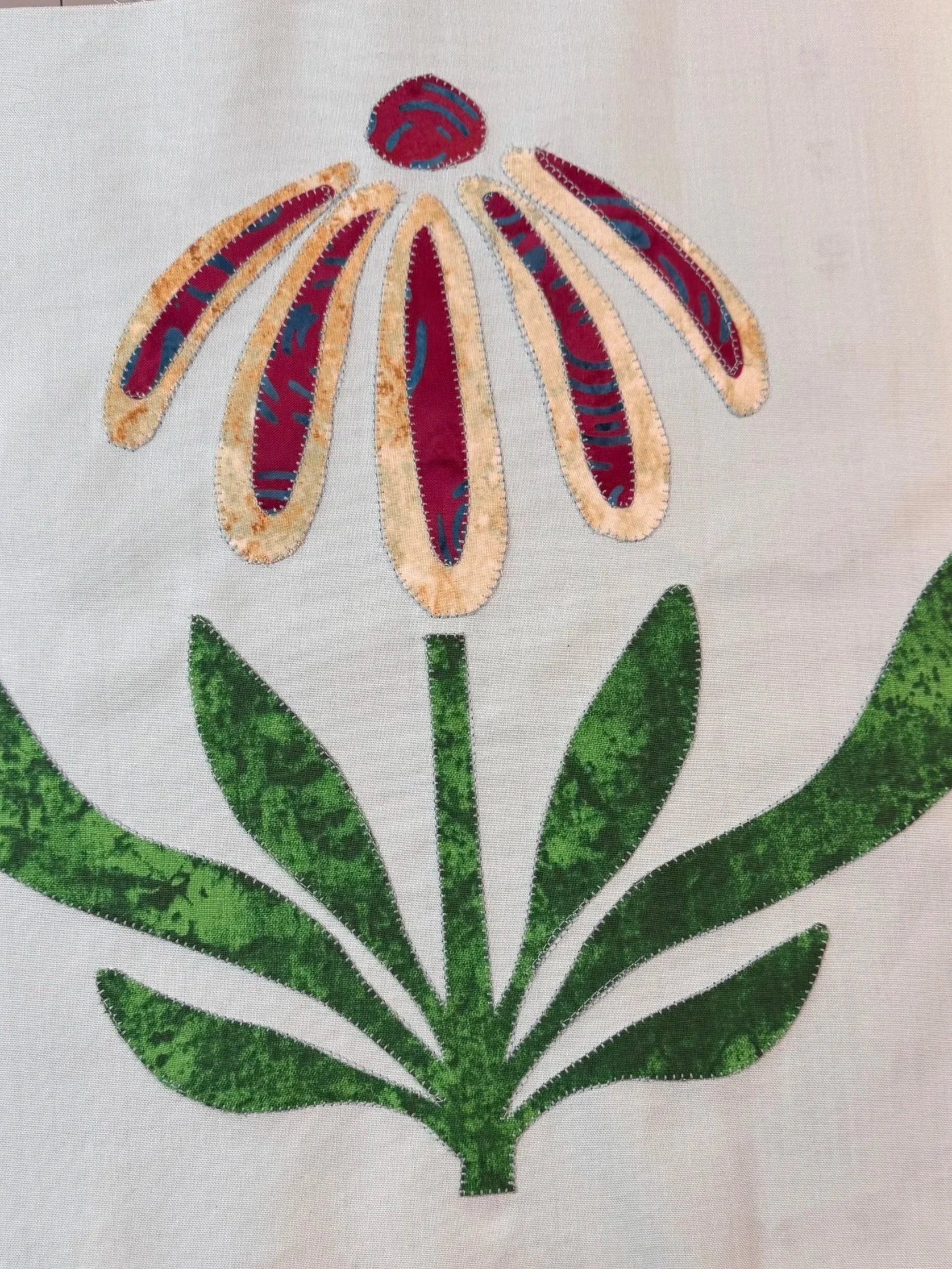 Colorful appliqué coneflower with green leaves on white fabric.