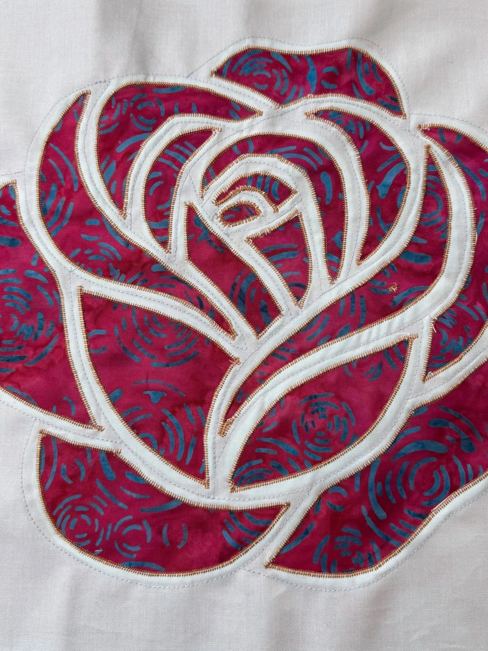 Burgundy and teal fabric appliqué rose with curved petals and stitched outlines.