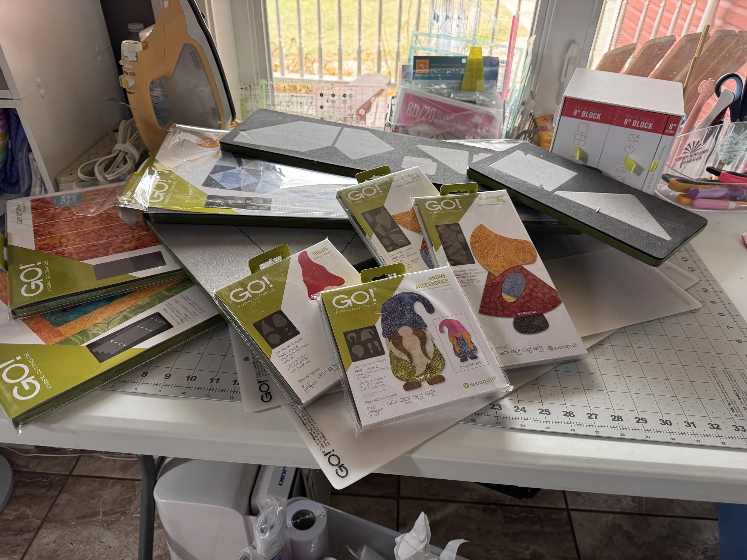 AccuQuilt GO! fabric cutting dies, quilting tools, and cutting mats arranged on a craft table.