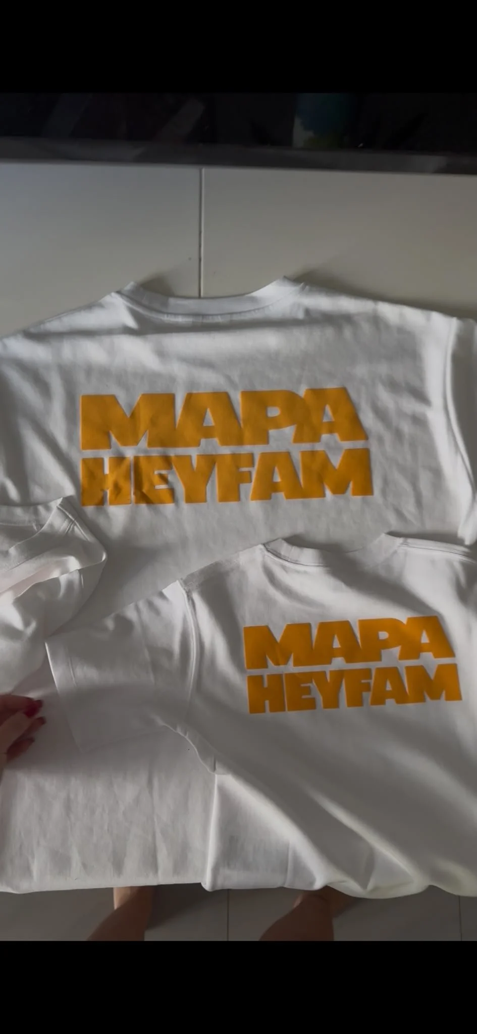 White T-shirts with orange text that reads 'MAPA HEYFAM' laid out on a table.