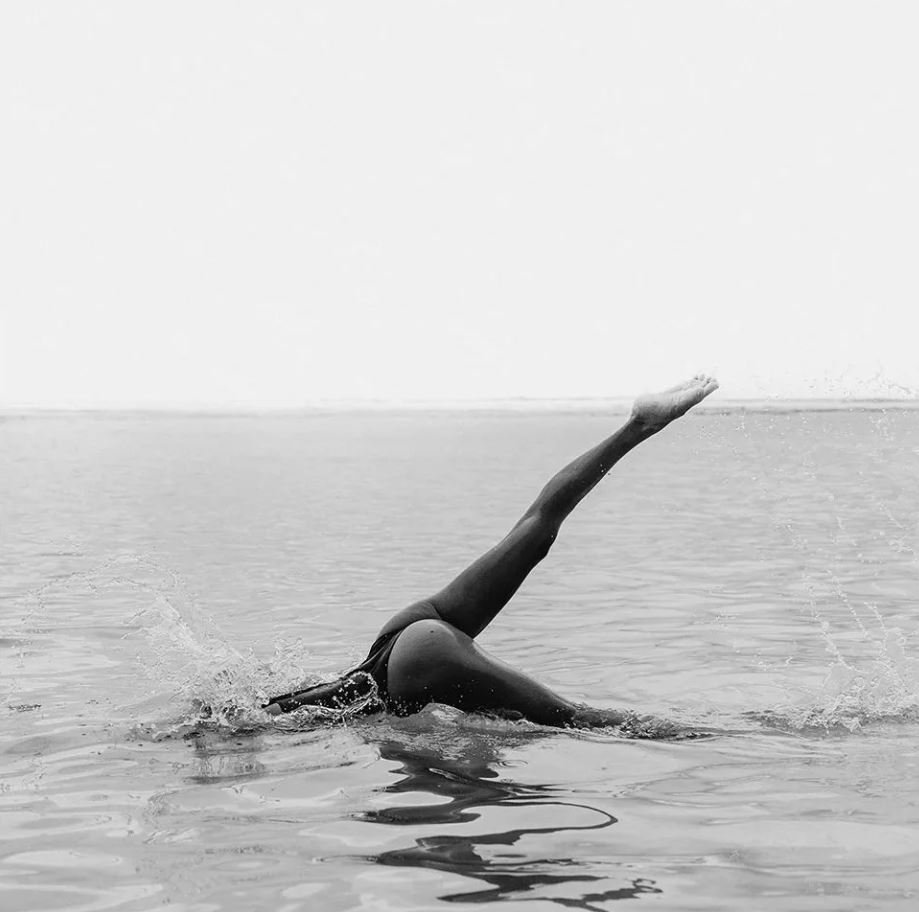 A person swimming in open water, performing a butterfly stroke with one arm extended upward and their head submerged.