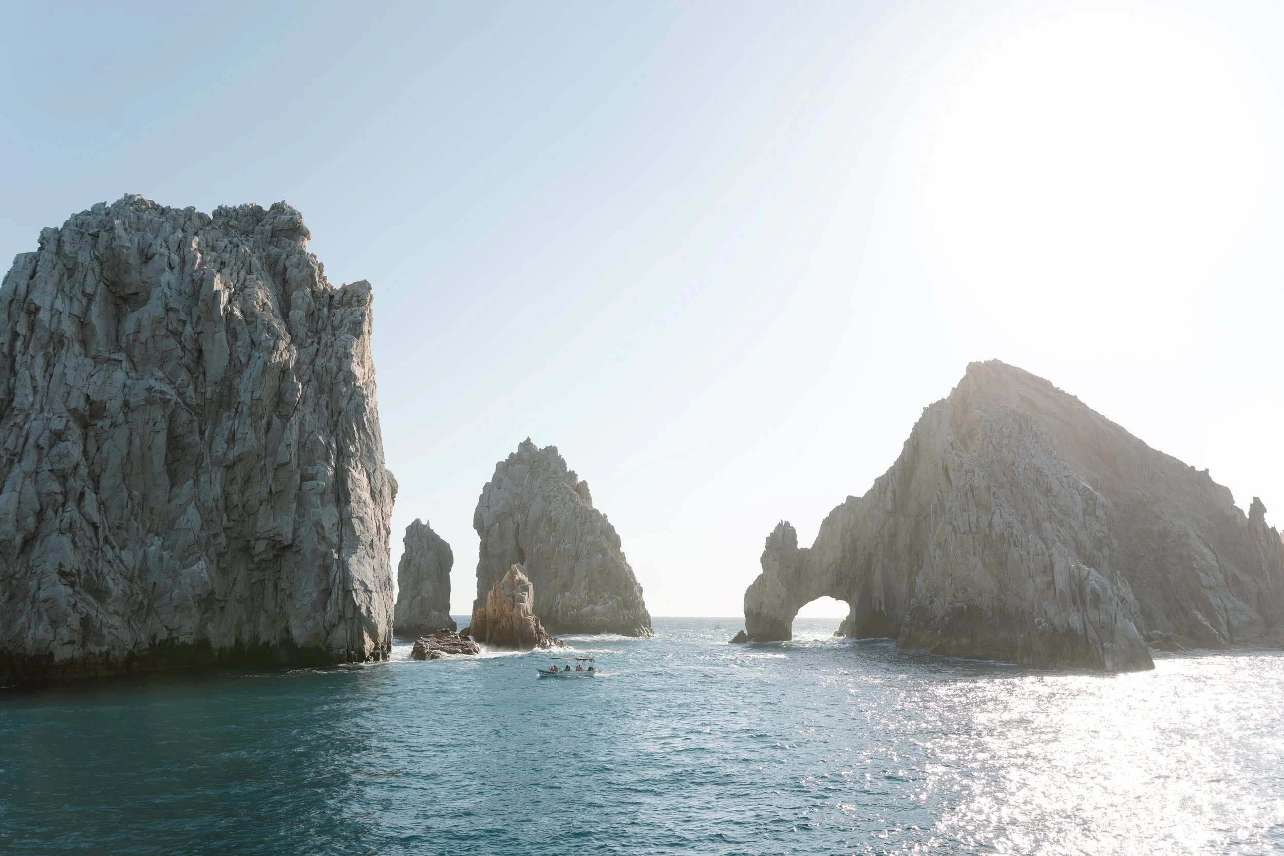 Sea arch formations with rocky cliffs on either side and a boat sailing in the water below, under a clear sky.