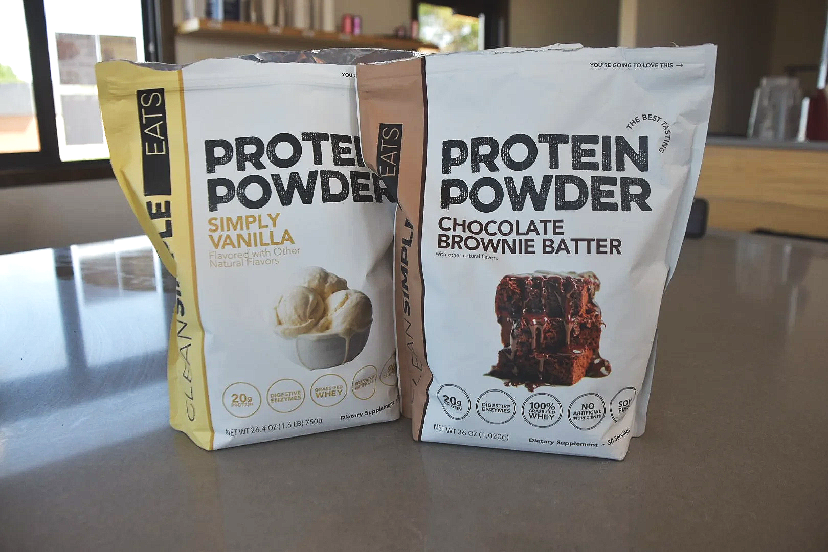 Two protein powder bags on a table, one vanilla flavored and the other chocolate brownie batter flavor.